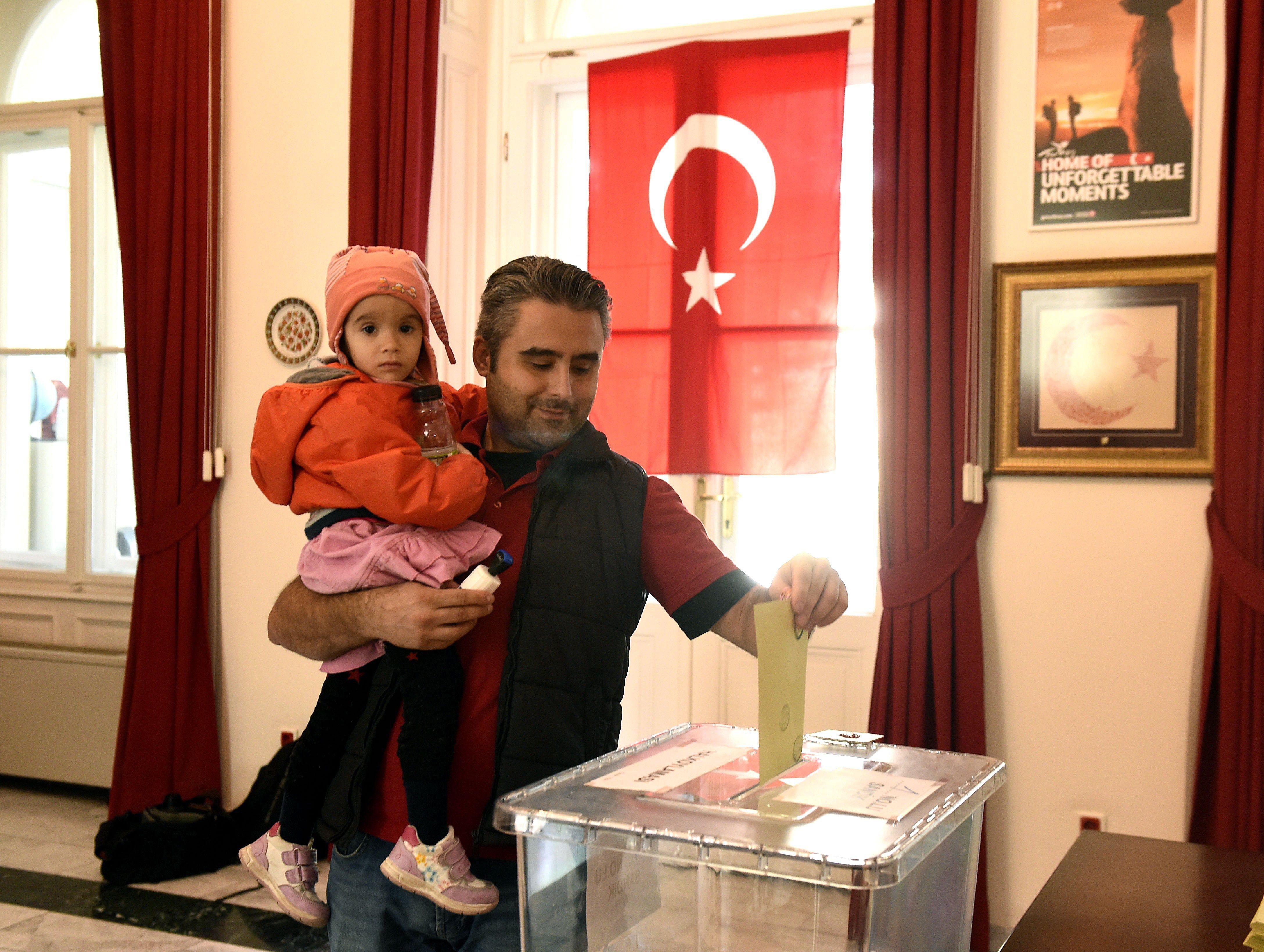 A Turkish citizen living in Hungary holds his daughter as he casts his vote in a Turkish referendum about amendments of the constitution to expand the presidential powers, in the Turkish embassy in Budapest, Hungary, Sunday, April 9, 2017, one week ahead of the referendum to be held in Turkey. (Noemi Bruzak/MTI via AP)