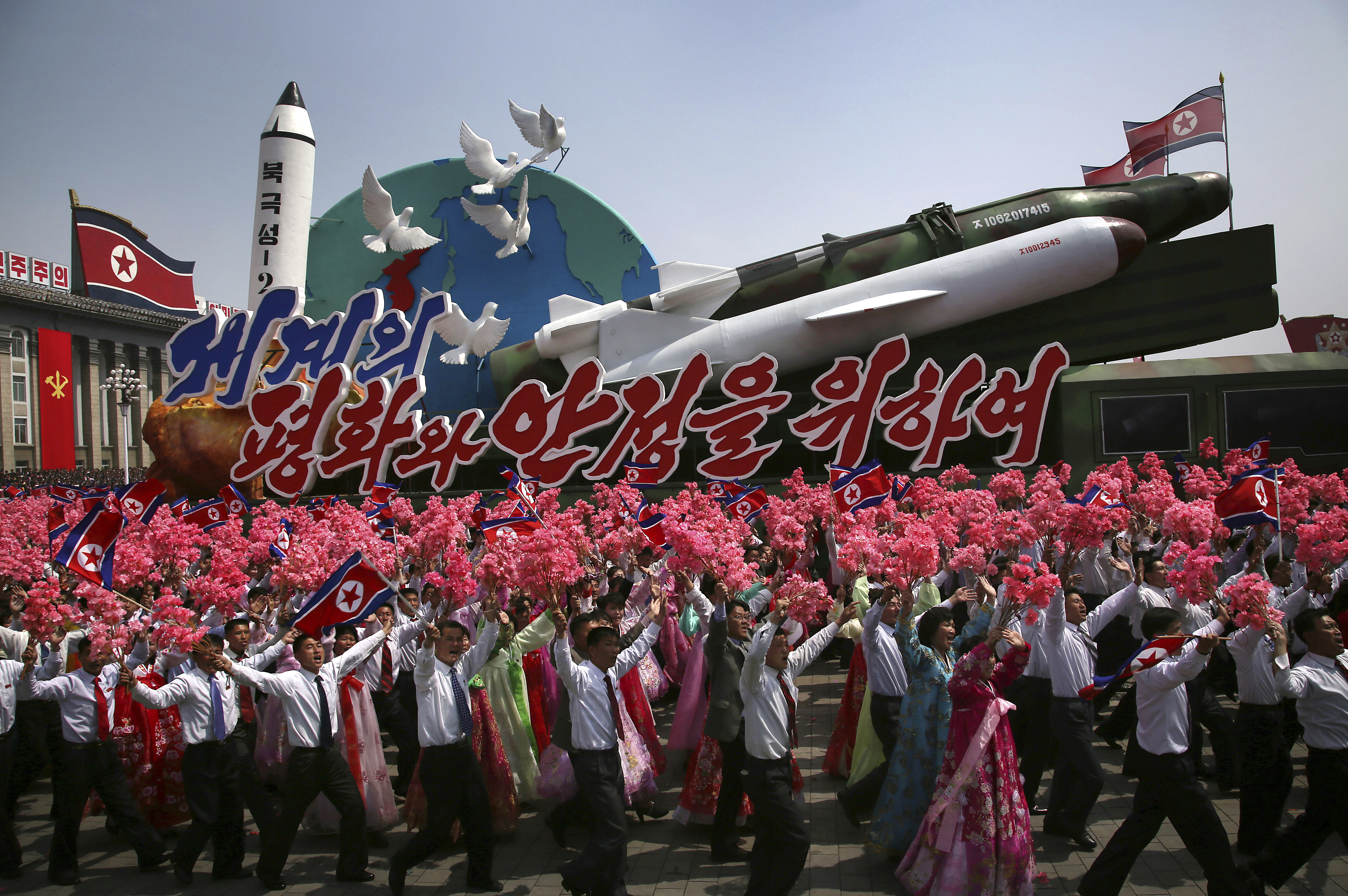 FILE - In this Saturday, April 15, 2017 file photo, North Korean men and women wave flags and plastic flowers as a float with model missiles and rockets with words that read 