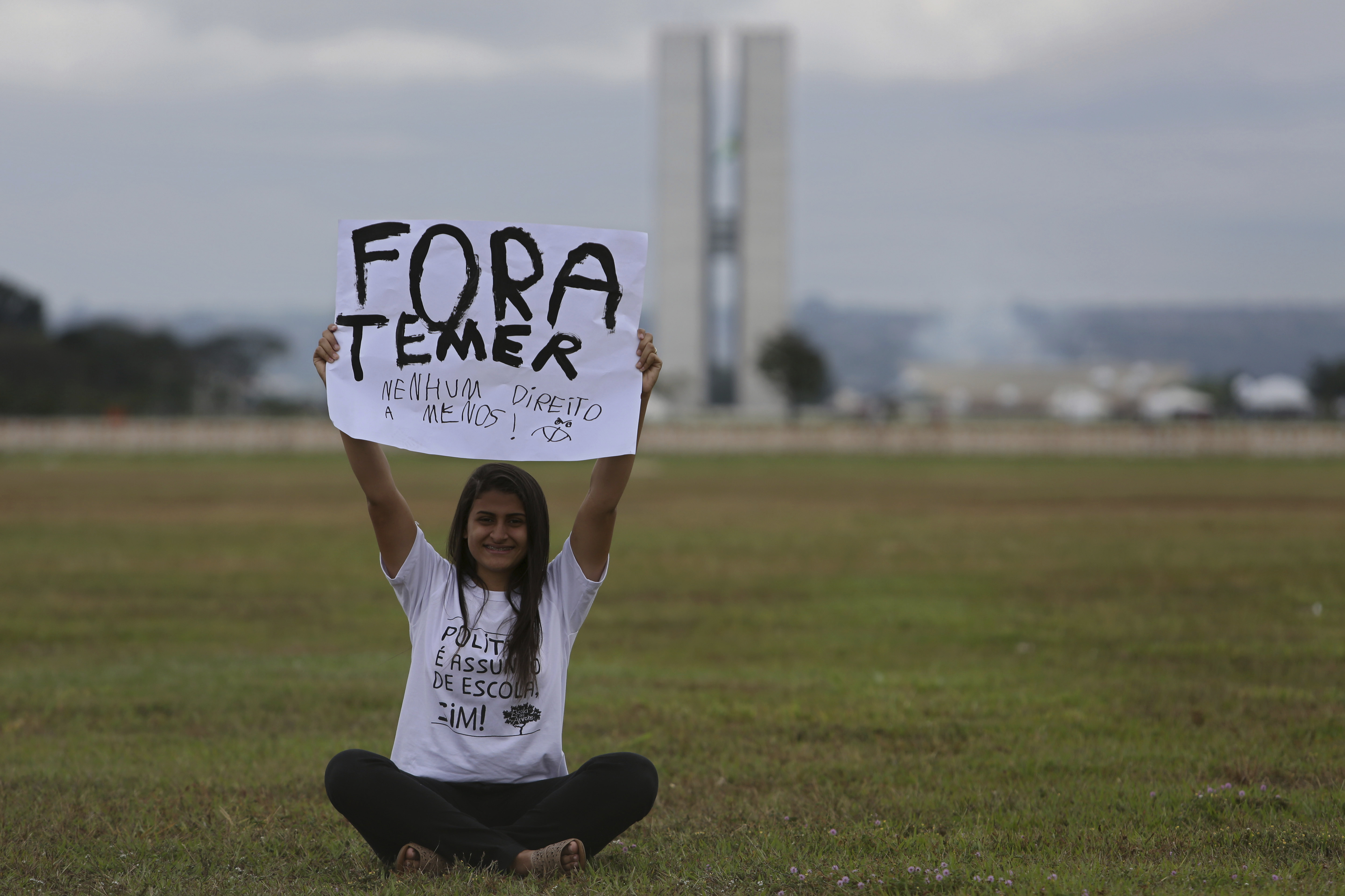 A woman holds up a poster with a message that reads in Portuguese; 
