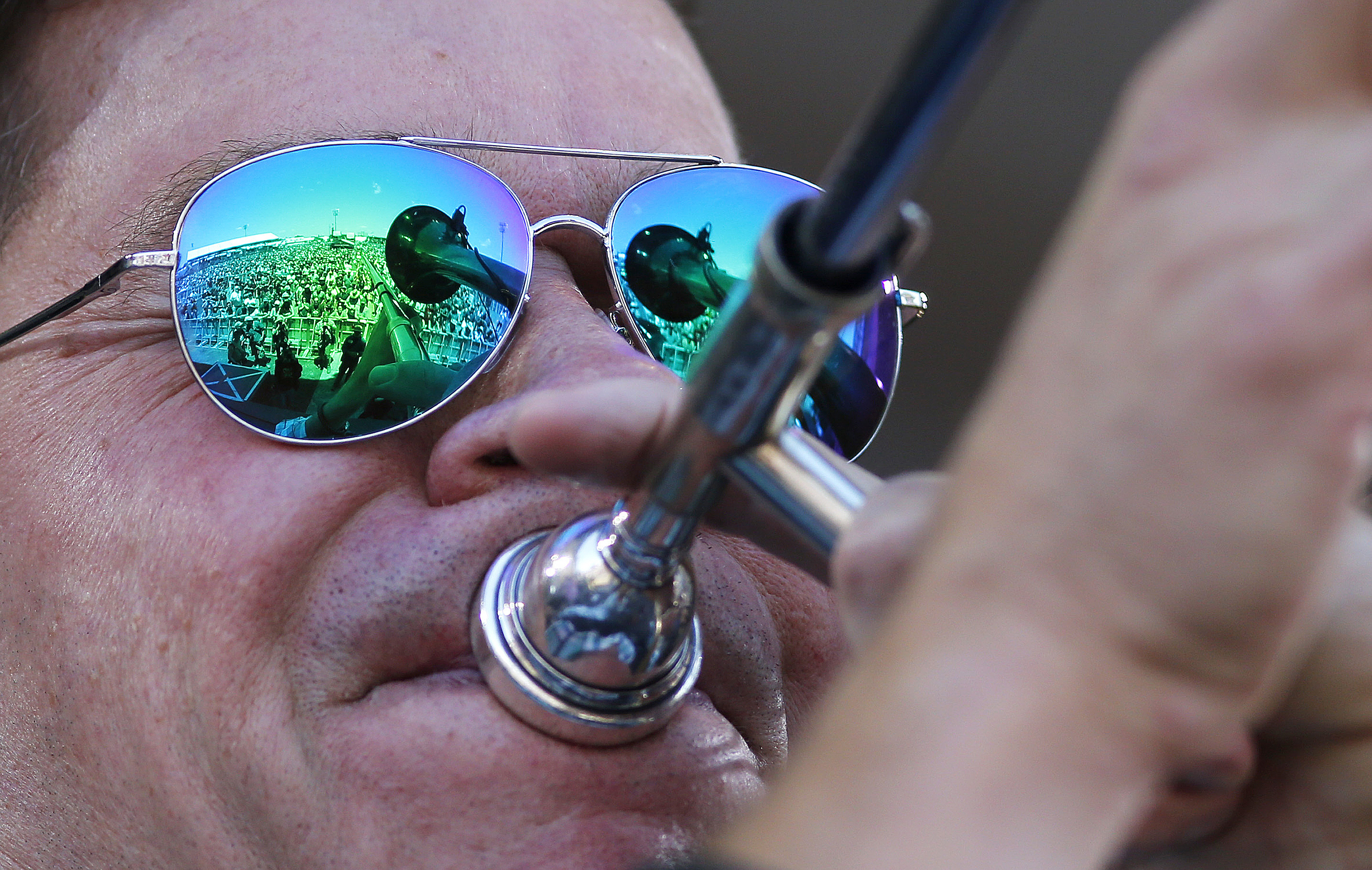 The trombone of Mark Mullins, of the brass funk rock band Bonerama, and the crowd at the Acura Stage, are seen in the reflection of his sunglasses as he performs with the band at the New Orleans Jazz and Heritage Festival in New Orleans, Friday, May 5, 2017. (AP Photo/Gerald Herbert)