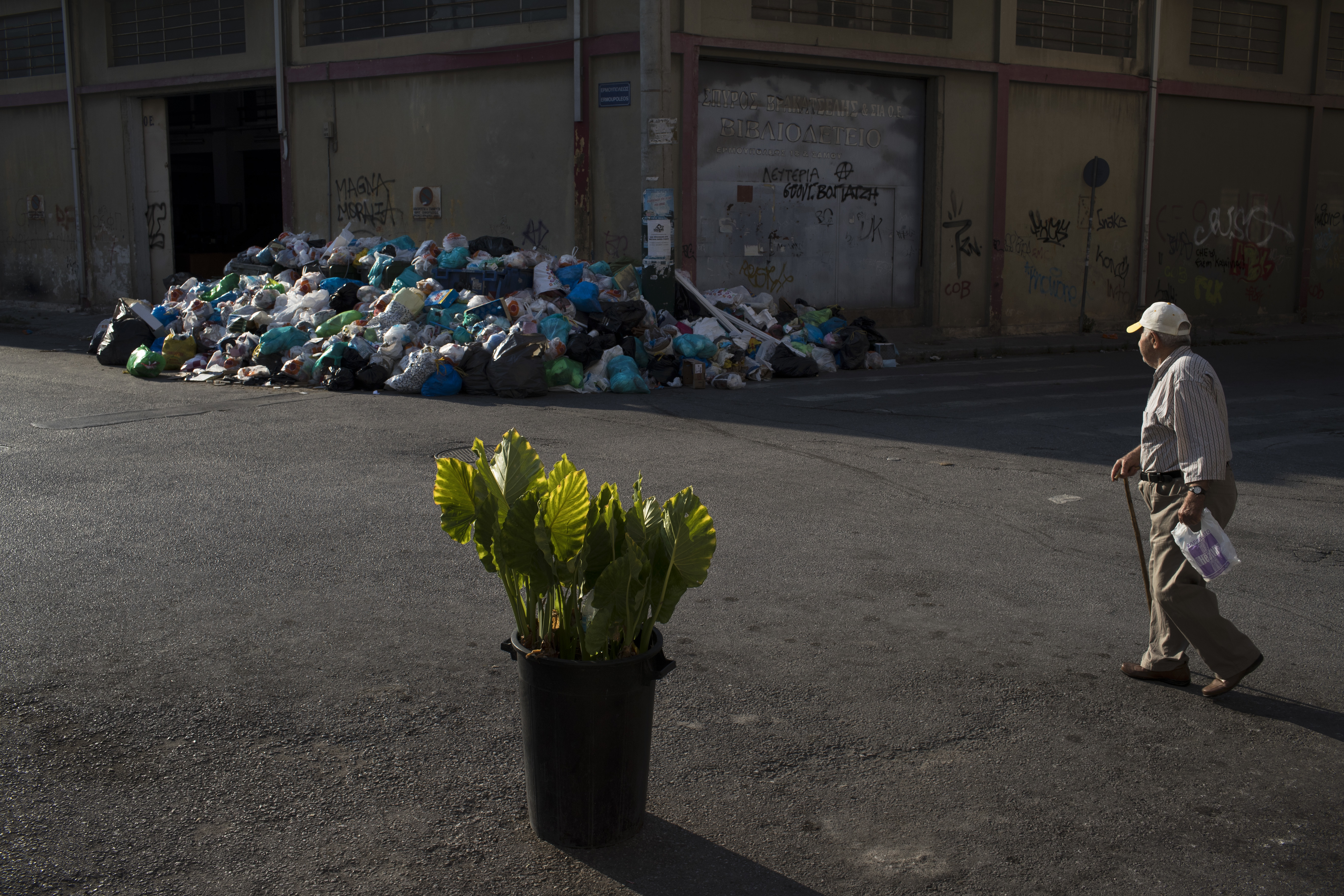 A man looks on a pile of trash as he walks behind a flower pot in Kaminia neighborhood of Piraeus, near Athens Tuesday,  June 27, 2017. Striking garbage collectors are on the 11-day of protest that left huge piles of trash around Athens. (AP Photo/Petros Giannakouris)