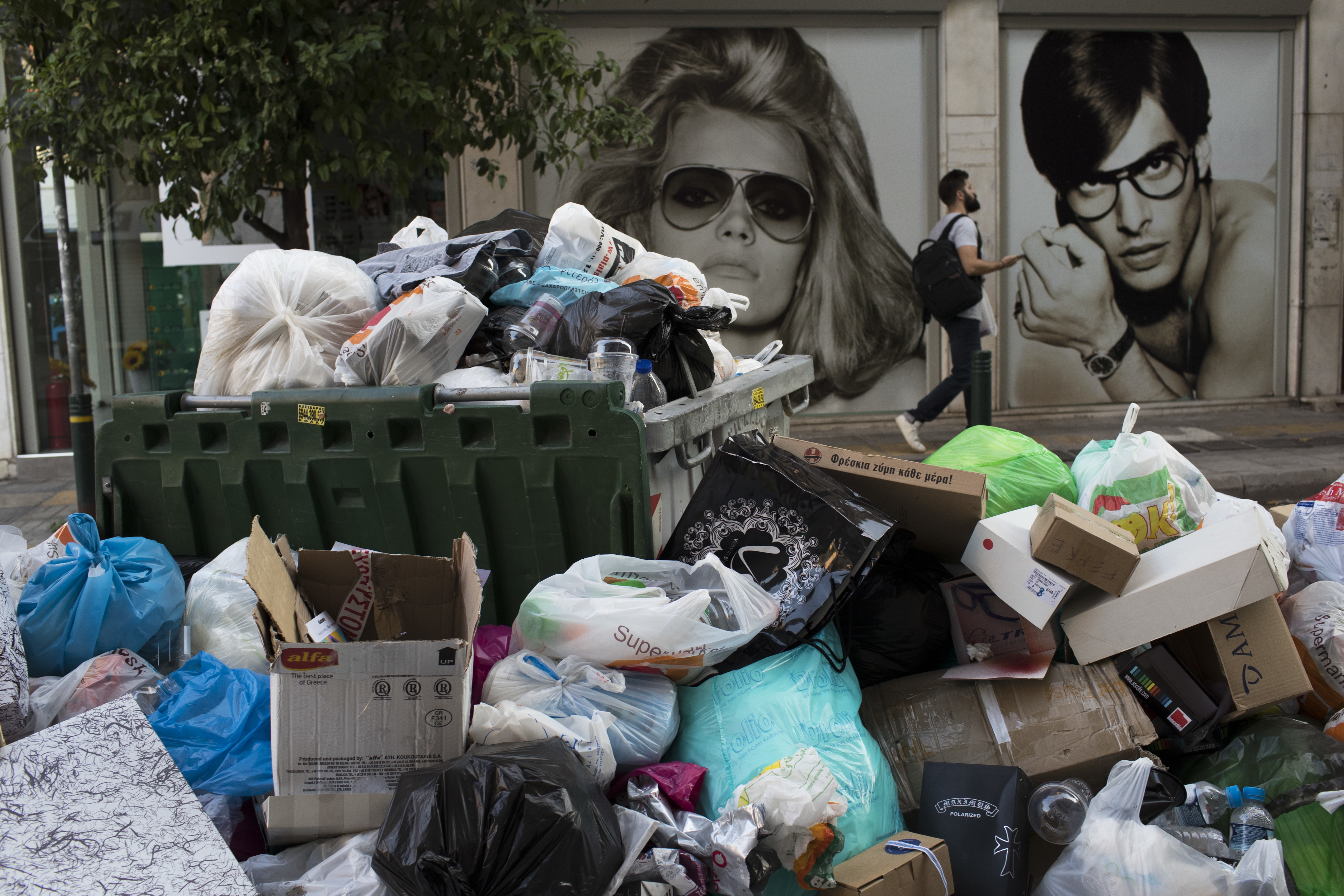 A man walk next an optical shop behind a pile of garbage in Piraeus, near Athens, on Monday, June 26, 2017. Municipality workers have been on strike for almost a week, hindering trash collection across the country. (AP Photo/Petros Giannakouris)