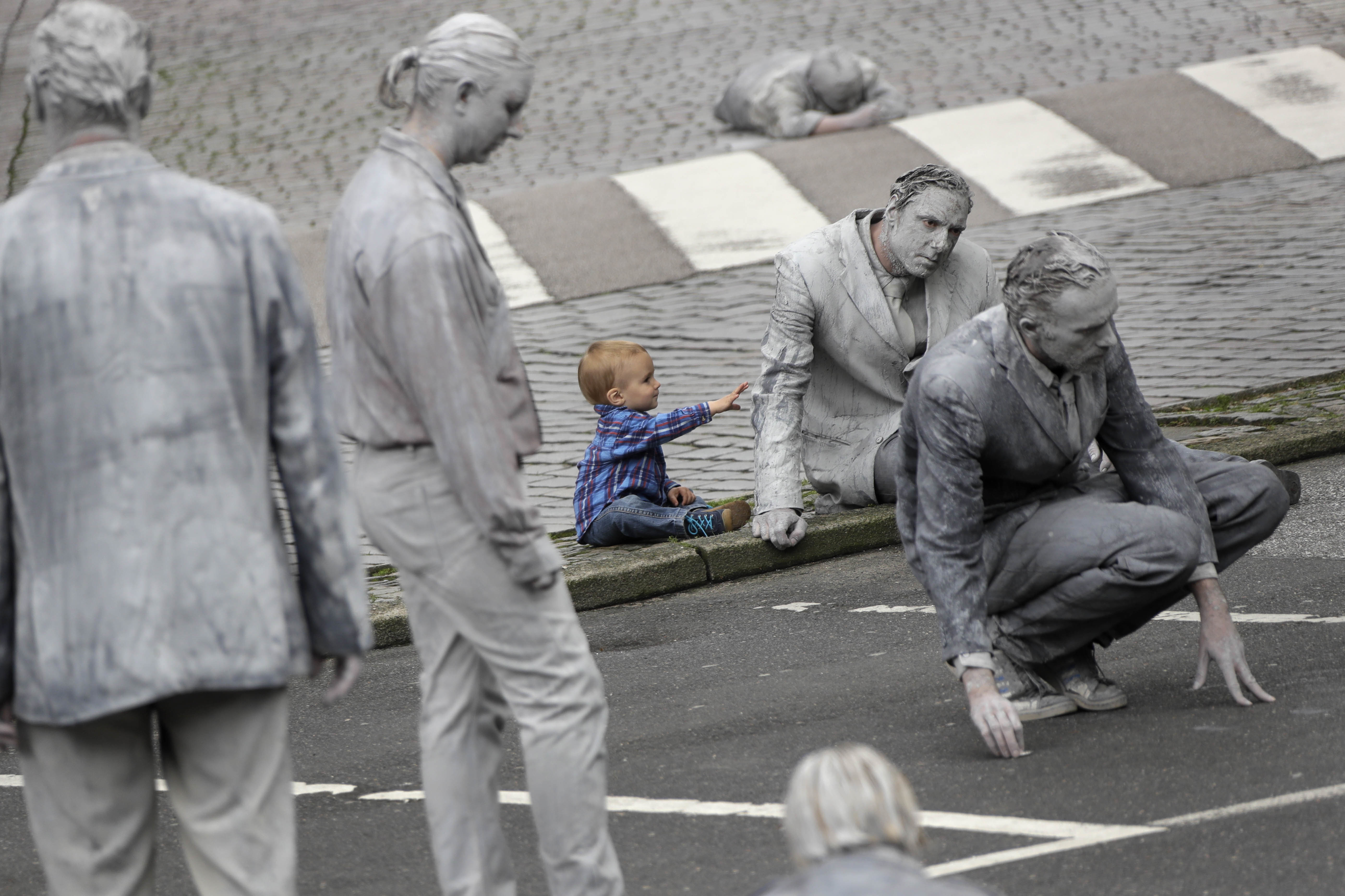 A small boy touches a participants of the performance '1000 GESTALTEN' with hundreds of people painted like clay figures moving slowly and silently through the streets of Hamburg to protest against the G-20 summit in Hamburg, northern Germany, Wednesday, July 5, 2017. The leaders of the group of 20 meet July 7 and 8. (AP Photo/Matthias Schrader)