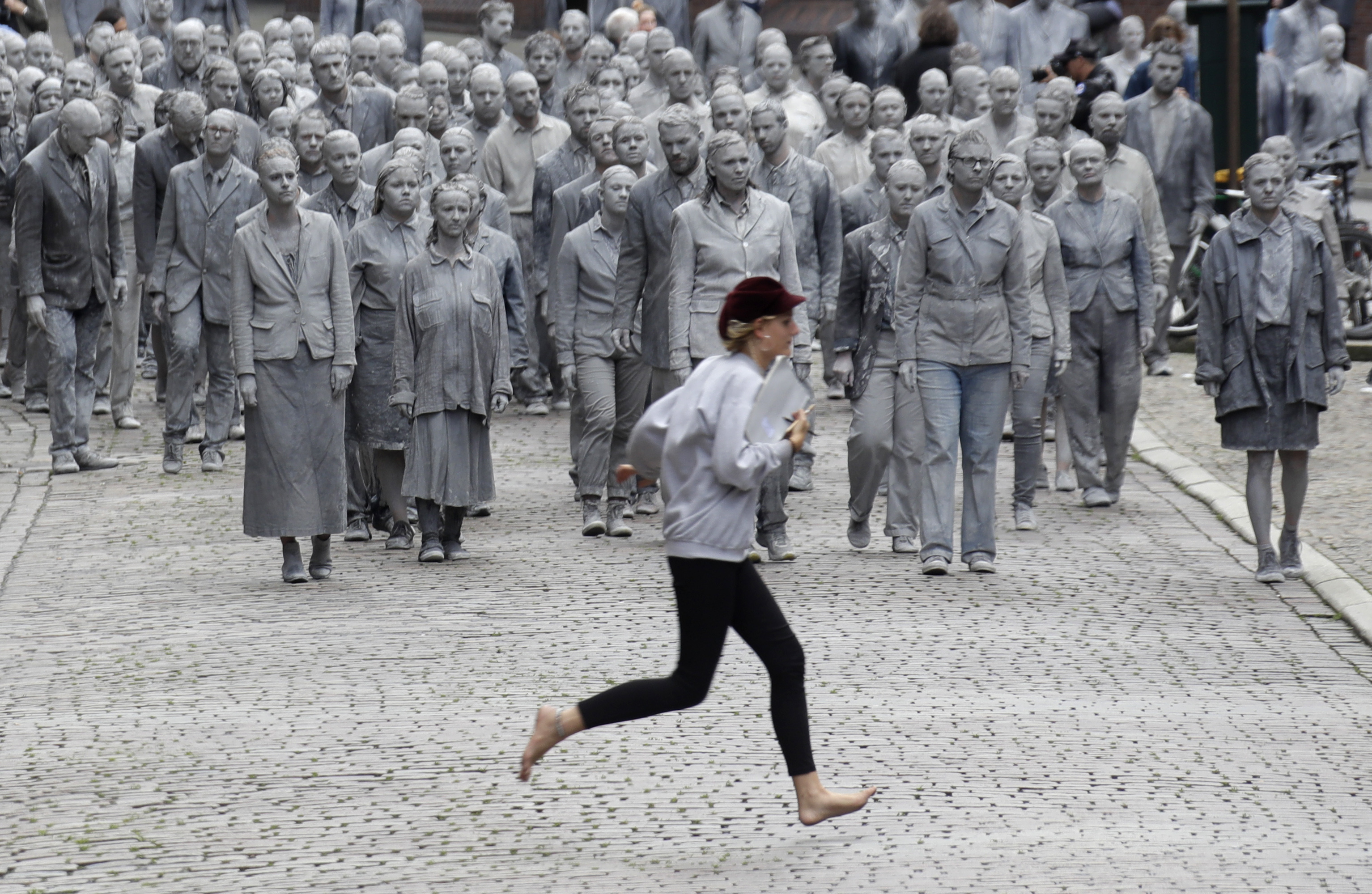 A woman crosses the street in front of the approaching performance '1000 GESTALTEN' with hundreds of people painted like clay figures moving slowly and silently through the streets of Hamburg to protest against the G-20 summit in Hamburg, northern Germany, Wednesday, July 5, 2017. The leaders of the group of 20 meet July 7 and 8. (AP Photo/Matthias Schrader)