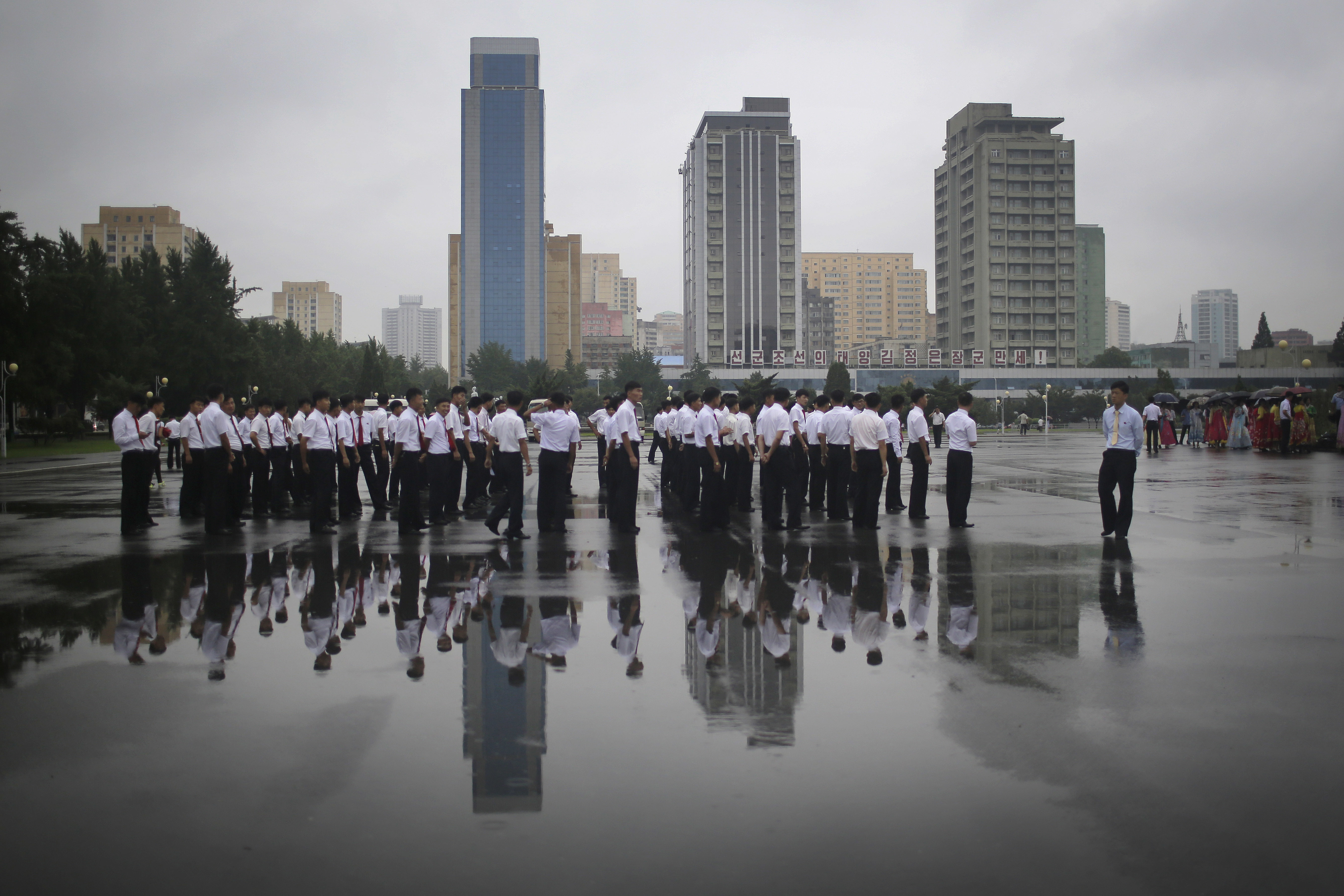 North Korean university students in their uniform are seen reflected in a rain puddle as they wait for the start of a mass dance on Thursday, July 27, 2017, in Pyongyang, North Korea as part of celebrations for the 64th anniversary of the armistice that ended the Korean War. (AP Photo/Wong Maye-E)