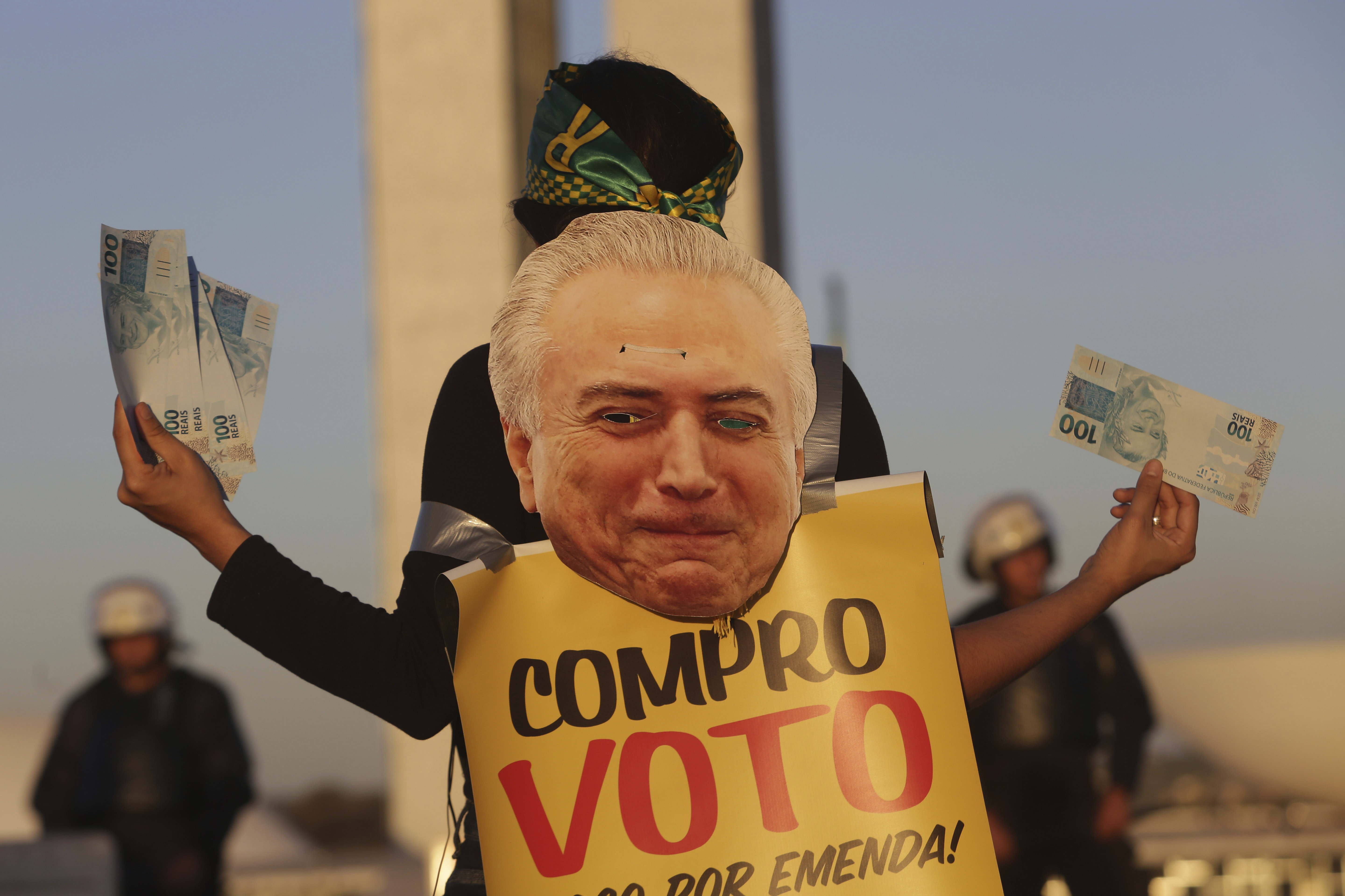 A woman holds fake Brazilian bank notes wearing a human billboard composed of an image of  President Michel Temer with a message that reads in Portuguese: 