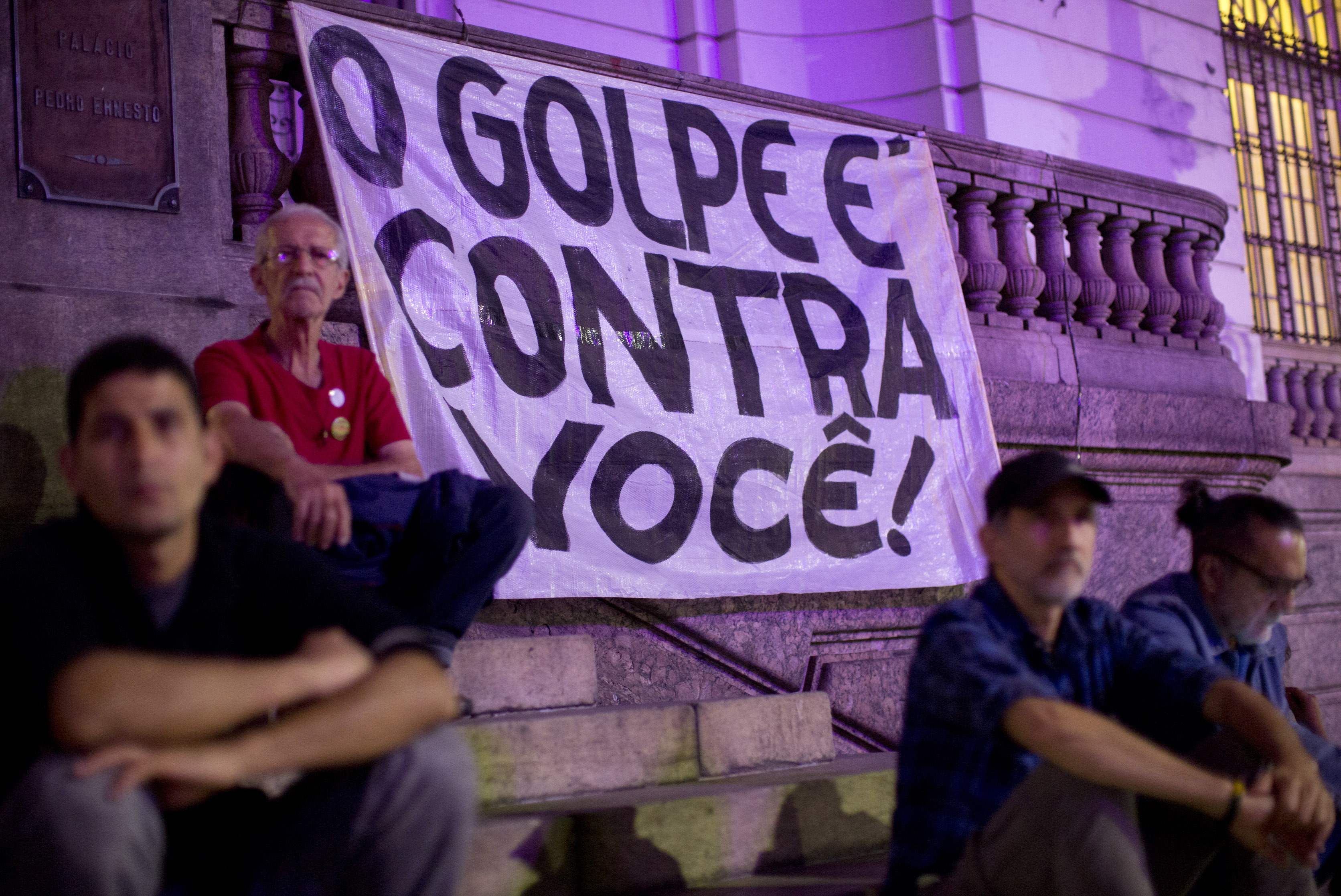 Demonstrators sit next to a banner that reads in Portuguese 