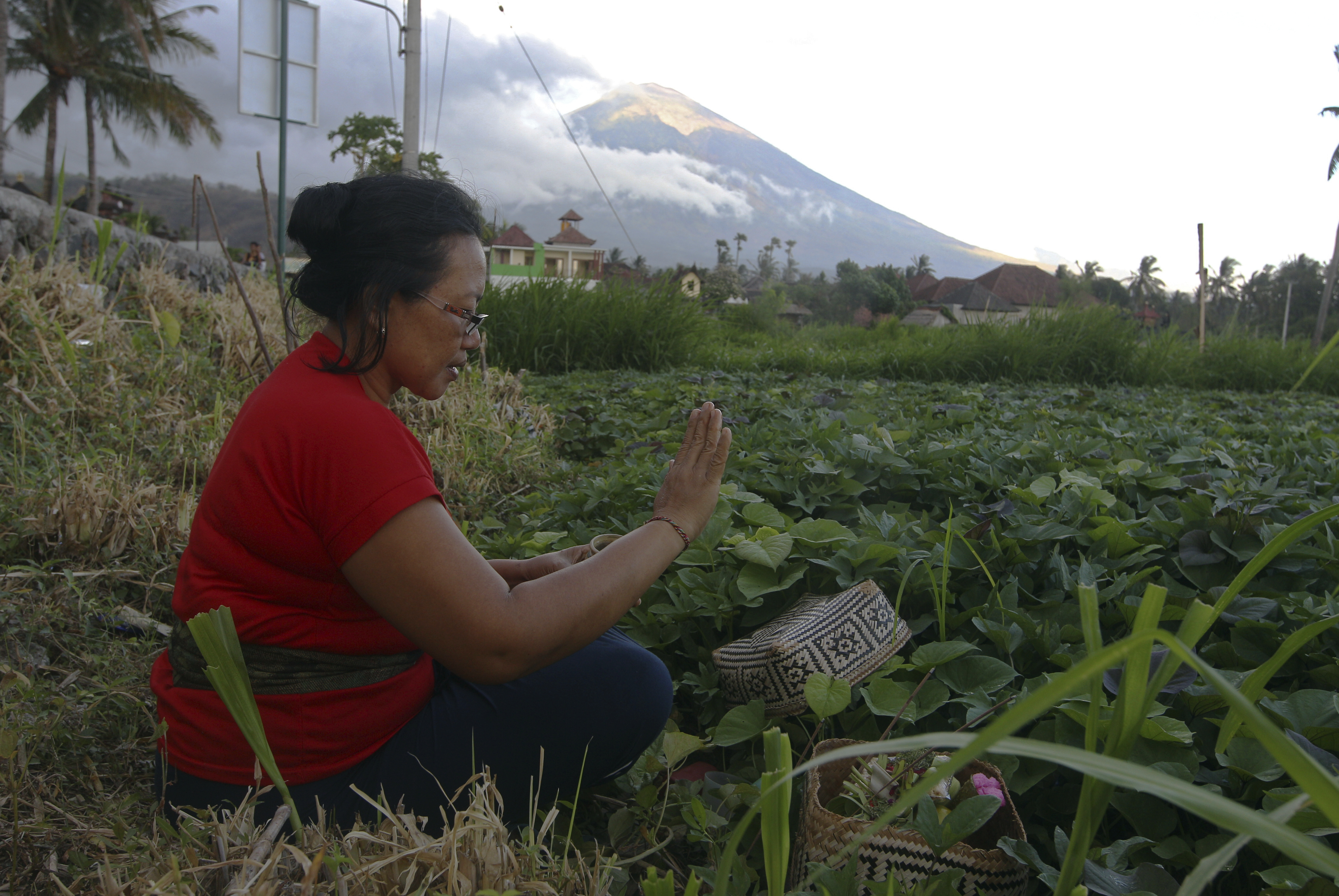 A woman prays at her plantation field with the Mount Agung volcano in the background in Karangasem, Bali, Indonesia, Saturday, Oct. 7, 2017. More than 140,000 people have fled from the surrounds of Mount Agung since authorities raised the volcano's alert status to the highest level on Sept. 22 after a sudden increase in tremors. It last erupted in 1963, killing more than 1,000 people. (AP Photo/Firdia Lisnawati)