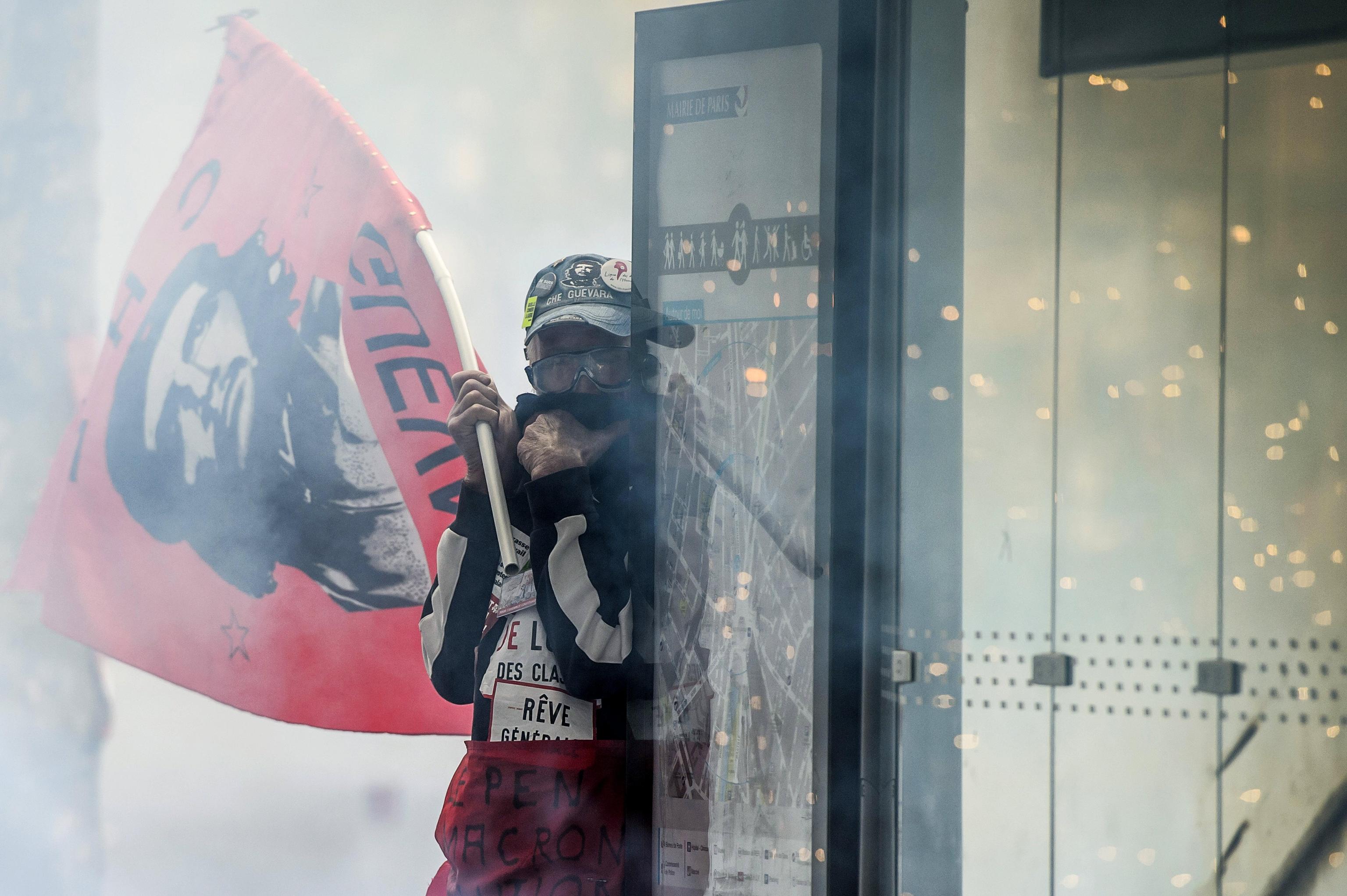 epa05939048 A protester takes cover while holding a Che Guevara flag as clashes erupt between protesters and French anti-riot police during a May Day demonstration against French far-right in Paris, France, 01 May 2017. Thousands of people demonstrated against the presence of Far-right Front National (FN) party candidate Marine Le-Pen for the second turn of the presidential elections. Labor Day or May Day is observed all over the world on the first day of the May to celebrate the economic and social achievements of workers and fight for laborers rights.  EPA/CHRISTOPHE PETIT TESSON