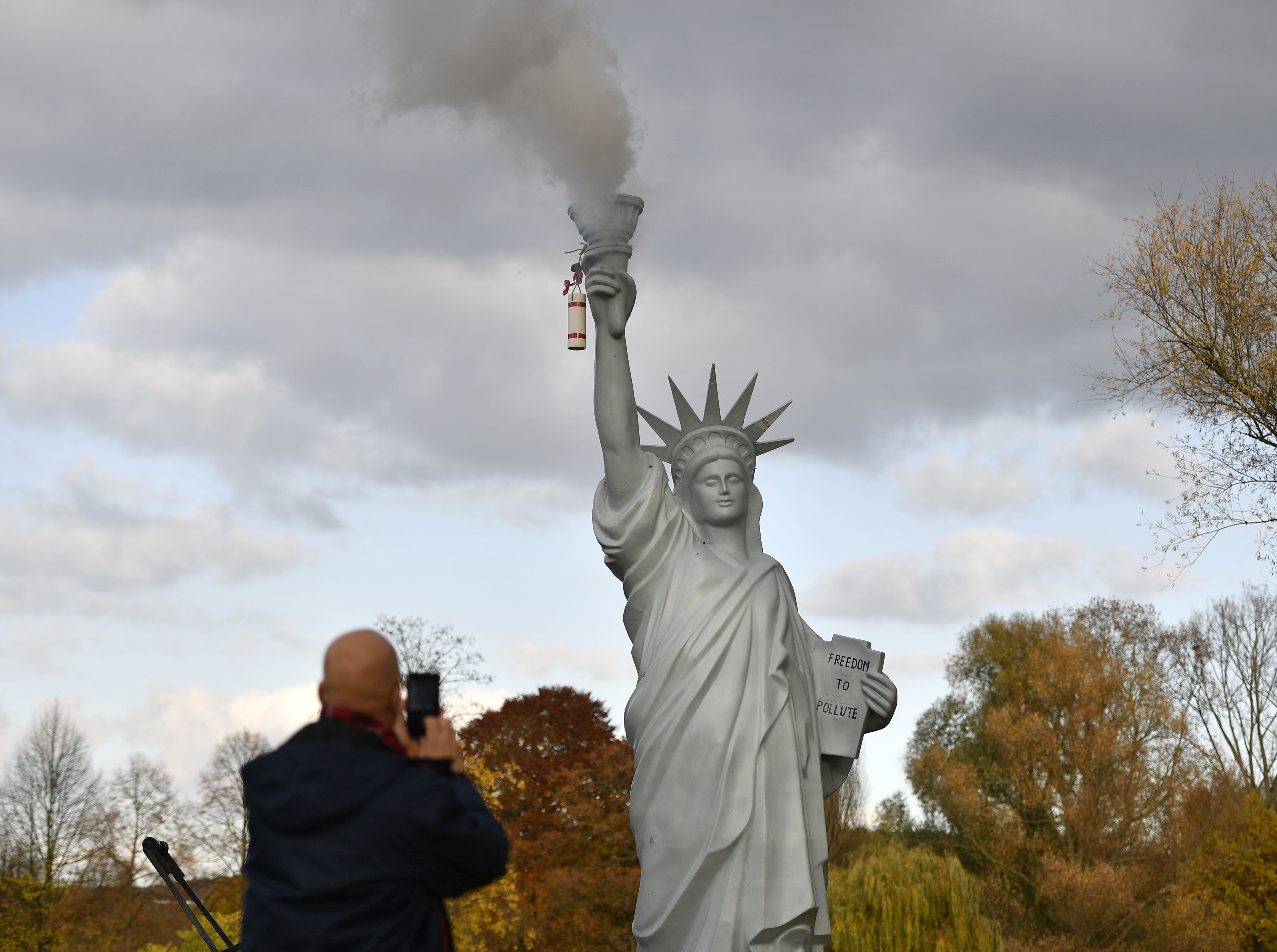 A man takes a picture of a replica of the Statue of Liberty by Danish artist Jens Galschiot, emitting smoke in a park outside the 23rd UN Conference of the Parties (COP) climate talks in Bonn, Germany, Friday, Nov. 17, 2017. (AP Photo/Martin Meissner)