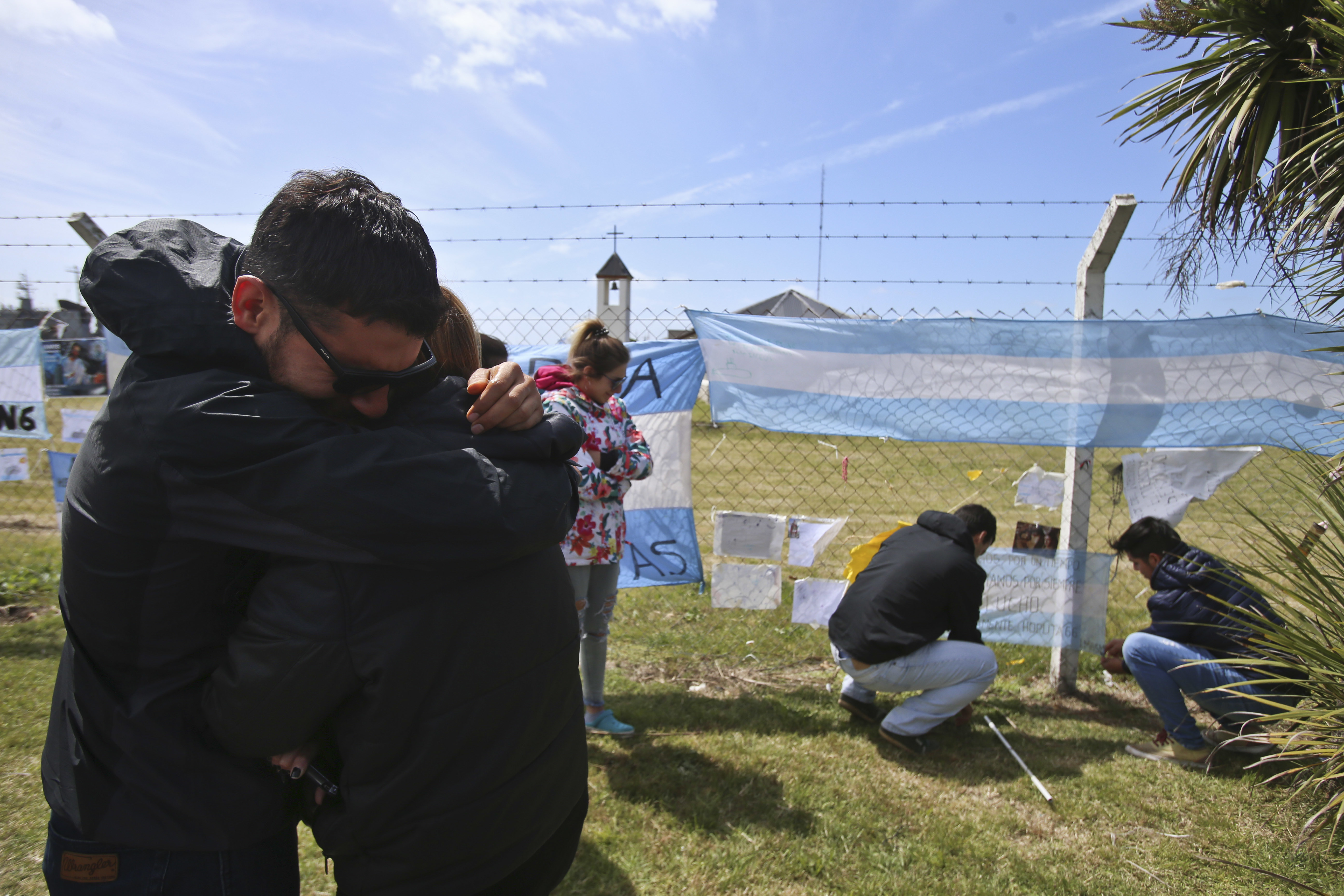 Relatives and friends of Alejandro Tagliaprieta, a crew member on the missing ARA San Juan submarine, embrace at the naval base where people hang flags and messages on the fence in Mar de Plata, Argentina, Friday, Nov. 24, 2017. The navy says an explosion occurred near the time and place where the sub went missing on Nov. 15. That's led some to give up hope. (AP Photo/Esteban Felix)