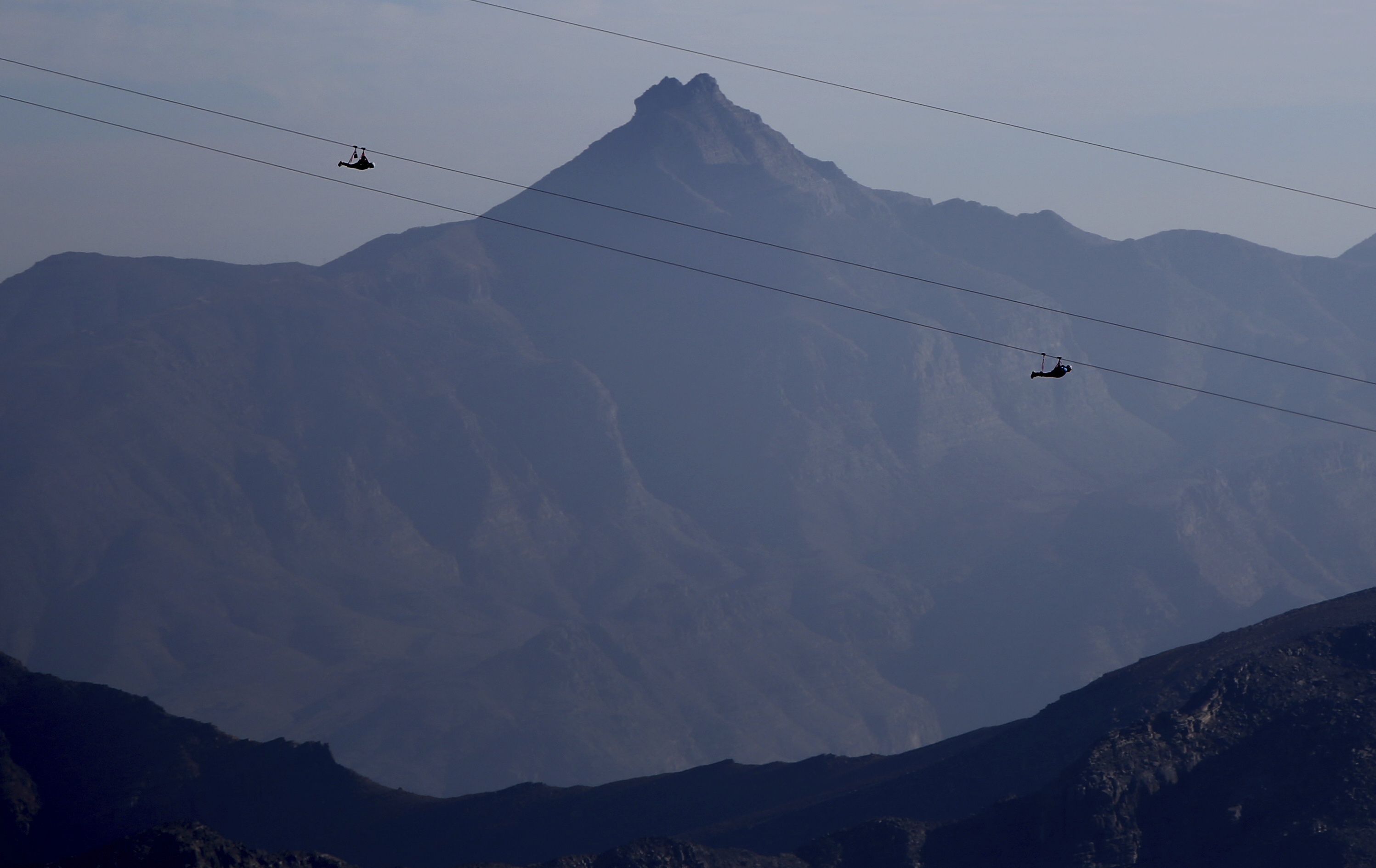 In this Wednesday, Jan. 31, 2018 photo, thrill-seekers descind from the UAE's highest mountain as they try out a new zip line, on the peak of Jebel Jais mountain, 25 kms (15.5 miles) north east of Ras al-Khaimah, United Arab Emirates. The UAE is claiming a new world record with the opening of the world's longest zip line, measuring 2.83 kilometers (1.76 miles) in length. Guinness World Records officials certified the zip line on Thursday, the same day the attraction opened to the public. (AP Photo/Kamran Jebreili)