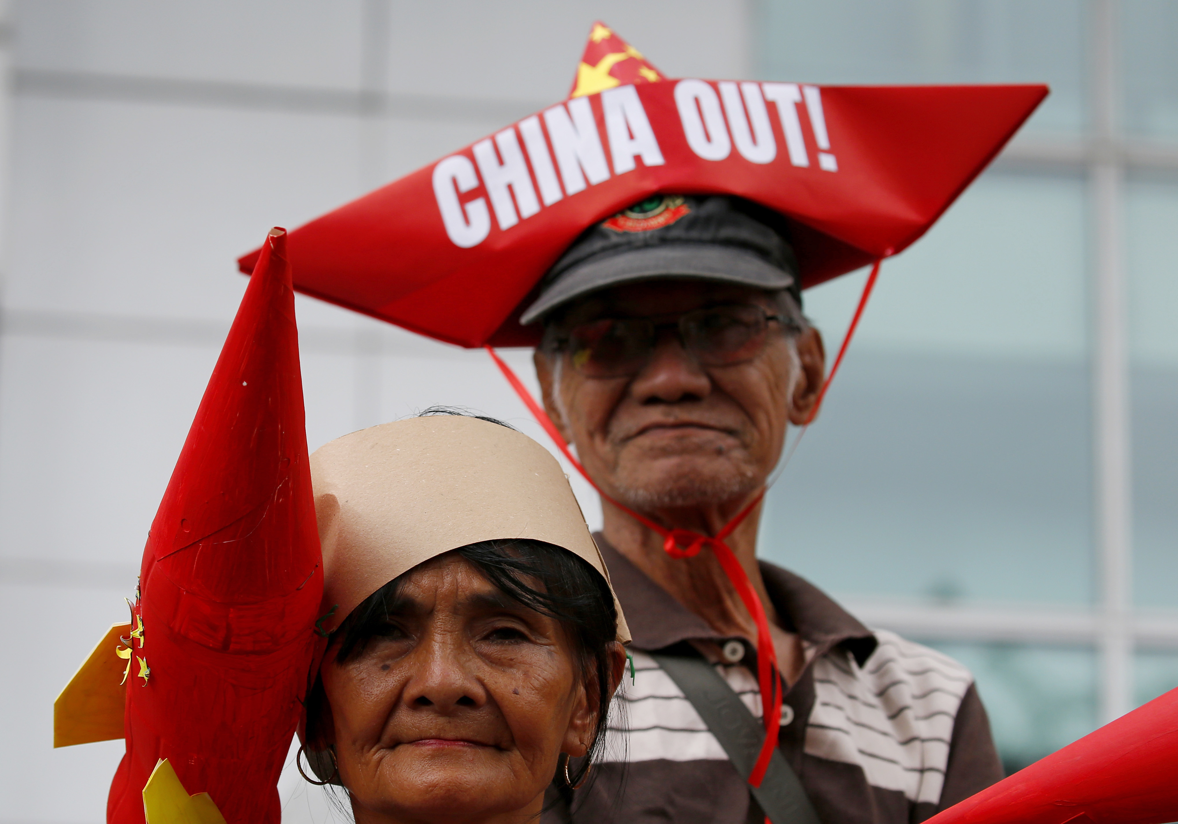 Protesters, one wearing boat-shaped paper hat and another with a mock missile, join other protesters in a rally at the Chinese Consulate to protest China's alleged continued militarization of the disputed islands in the South China Sea known as Spratlys Saturday, Feb. 10, 2018 in the financial district of Makati city east of Manila, Philippines. The protesters also denounced President Rodrigo Duterte's inaction over China's continued build up of military facilities and structures at the disputed islands. (AP Photo/Bullit Marquez)