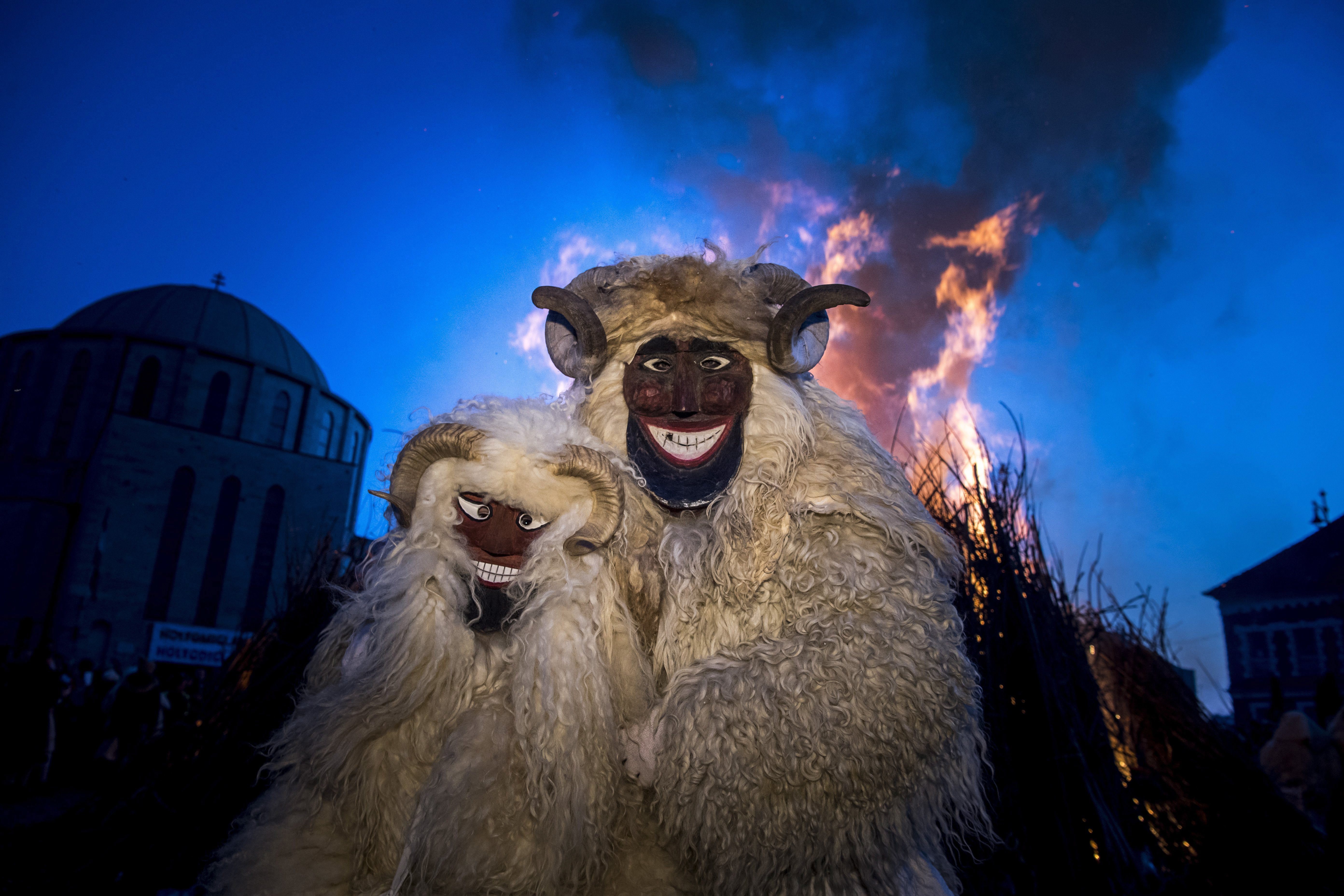 Revellers wearing a sheep wool costume with horns and a mask stand in front of a bonfire in Mohacs, some 210 kms south of Budapest, during the traditional carnival parade of the town Sunday, Feb. 11, 2018. The carnival parade of people dressed in similar costumes and frightening wooden masks, using various noisy wooden rattlers is traditionally held on the seventh weekend before Easter to drive away winter, and is a revival of a legend, which says the ethnic Croats crossed the river to ambush the Osmanli Turkish troops, who escaped in panic seeing the terrifying figures during the Turkish occupation of Hungary. (Zsolt Szigetvary/MTI via AP)