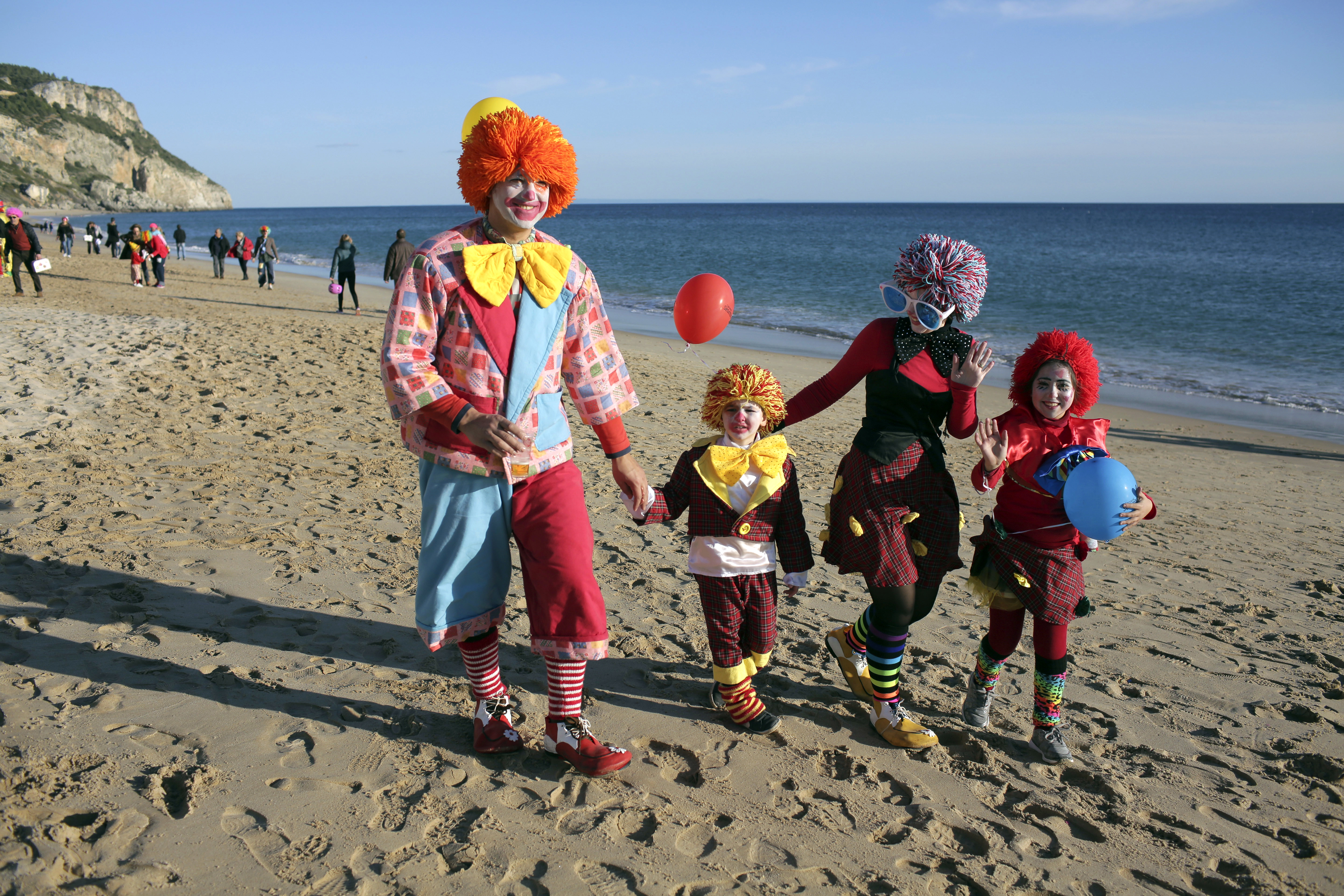 A family waves to the camera while walking on the beach after taking part in the Carnival Clowns' Parade along the waterfront in Sesimbra, south of Lisbon, Monday, Feb. 12, 2018. Every year on Carnival Monday thousands dress as clowns to take part in the fishing town's parade. (AP Photo/Armando Franca)