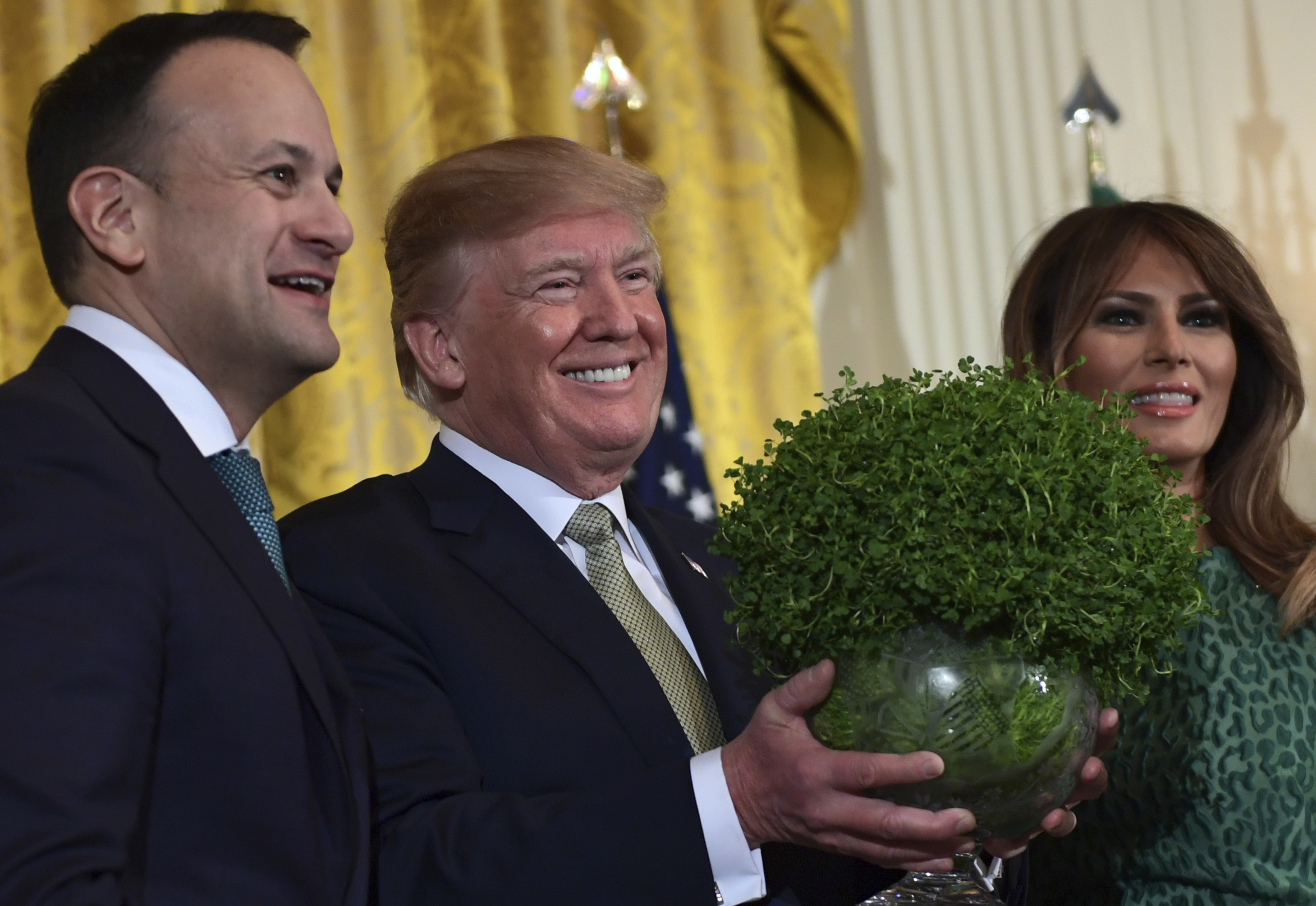 President Donald Trump, center, smiles as he is presented with a traditional gift of a bowl of shamrocks from Irish Prime Minister Leo Varadkar, left, during a St. Patrick's Day reception in the East Room of the White House in Washington, Thursday, March 15, 2018. First lady Melania Trump stands at right. (AP Photo/Susan Walsh)