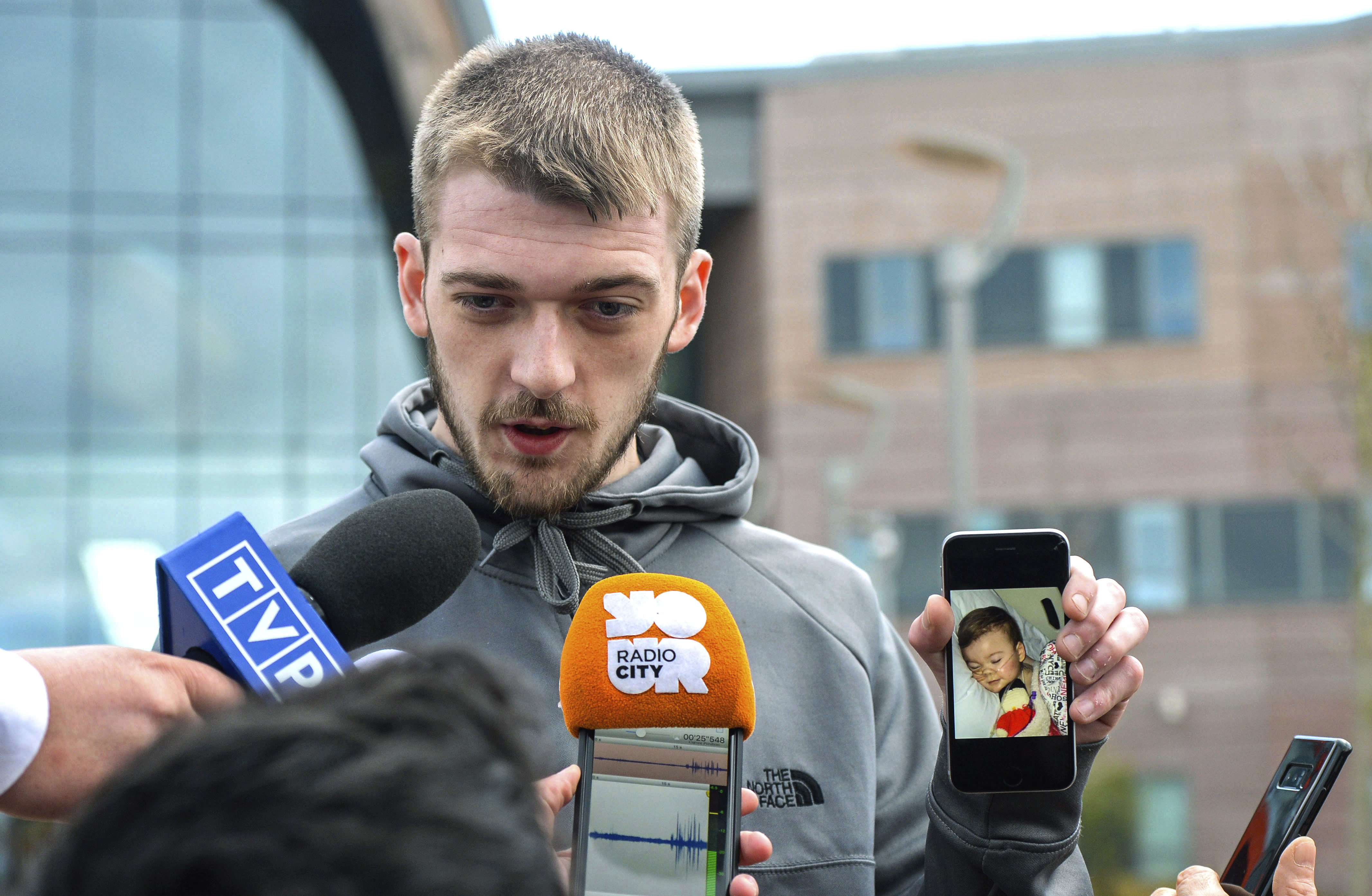 FILE - In this Thursday April 26, 2018 file photo Tom Evans holds up his phone showing a photo of his son Alfie as he speaks to the media outside Alder Hey Children's Hospital where the 23-month-old who has been at the centre of a life-support treatment dispute, in Liverpool, England. Kate James and Tom Evans, the parents, said on Facebook that 23-month-old Alfie Evans, who had an incurable degenerative brain condition and was at the center of a legal battle over his treatment, died early morning Saturday April 28, 2018. (Peter Byrne/PA via AP, File)