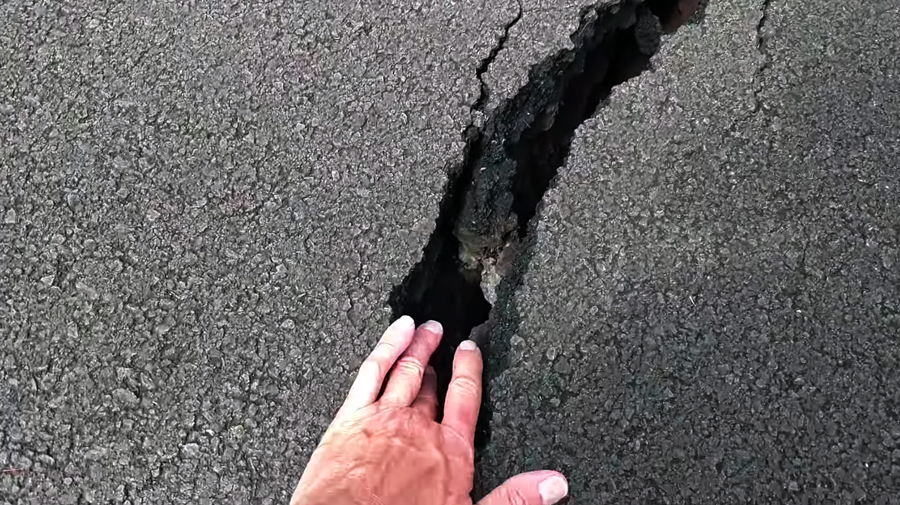 In this photo taken from video Scott Wiggers, of Apau Hawaii Tours, feels warmth from a fissure in a road in the Leilani Estates subdivision near Pahoa on the island of Hawaii Monday, May 7, 2018. Kilauea volcano has destroyed more than two dozen homes since it began spewing lava hundreds of feet into the air last week, and residents who evacuated don't know how long they might be displaced. The decimated homes were in the Leilani Estates subdivision, where molten rock, toxic gas and steam have been bursting through openings in the ground created by the volcano. (Scott Wiggers/Apau Hawaii Tours via AP)