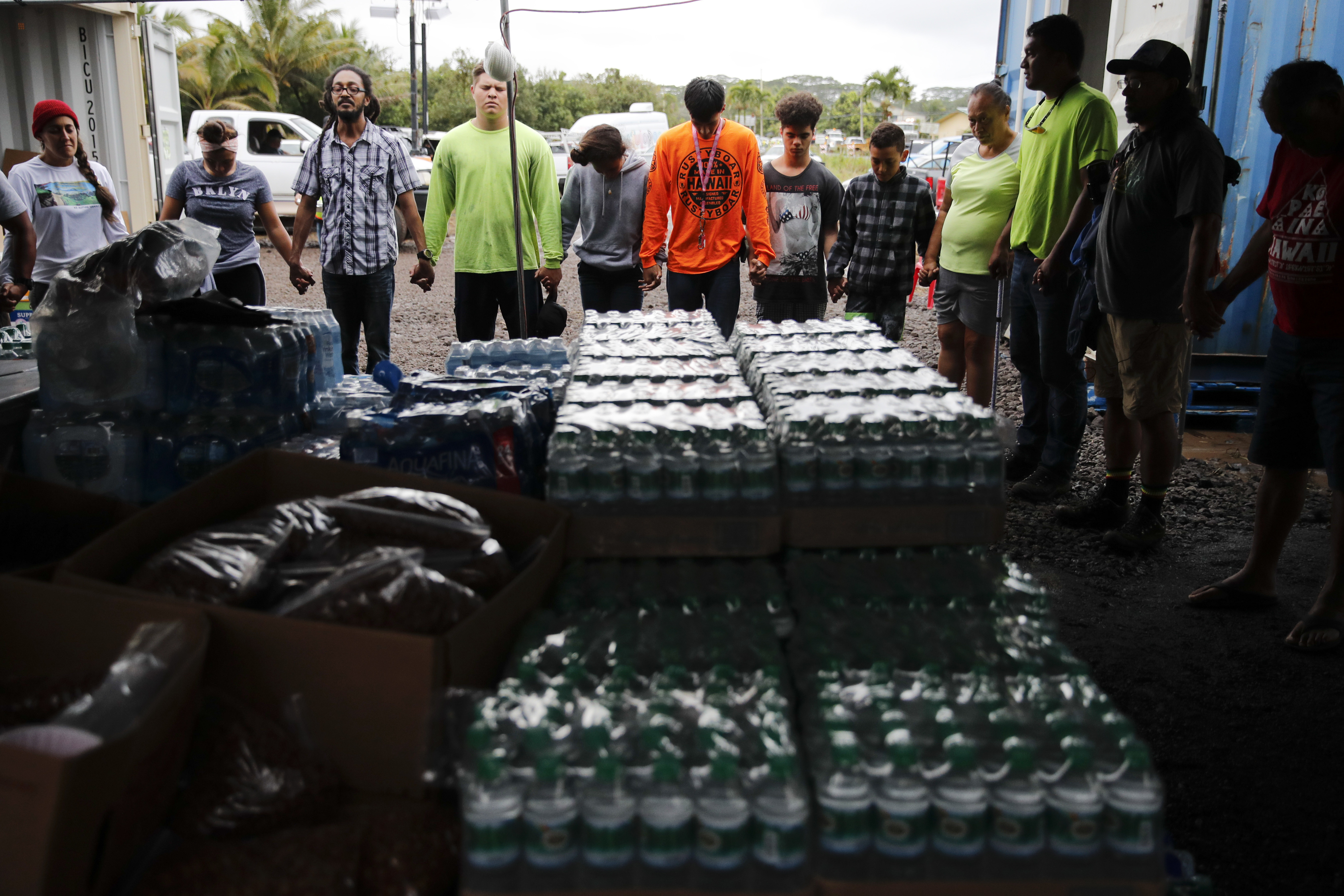 Volunteers and evacuees hold in hands while praying before serving dinner at a makeshift donation center Tuesday, May 8, 2018, in Pahoa, Hawaii. Hawaii County officials have issued a cellphone alert warning residents of a subdivision to immediately evacuate after two new lava fissures opened in a neighboring community. (AP Photo/Jae C. Hong)