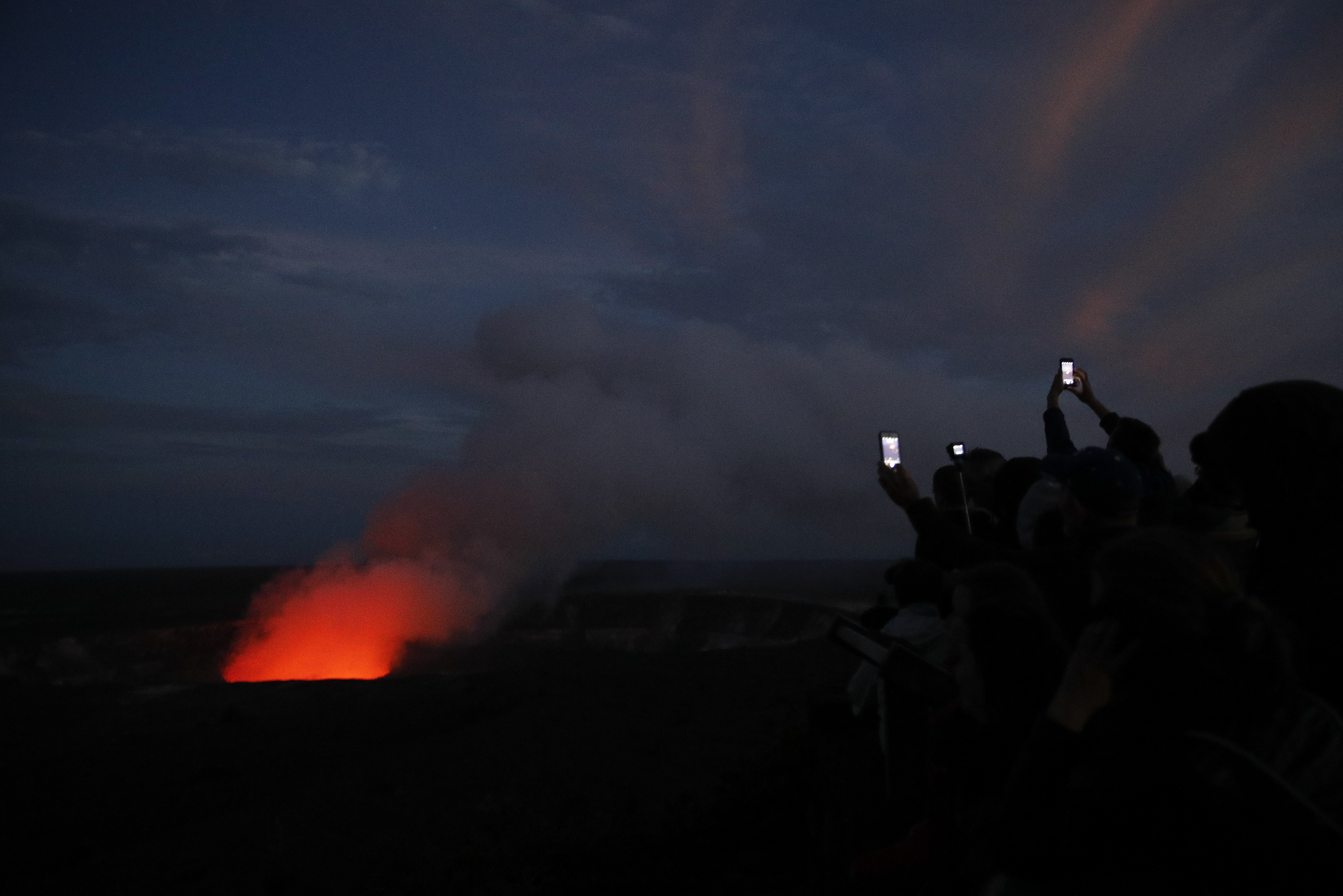 Visitors take pictures as Kilauea's summit crater glows red in Volcanoes National Park, Hawaii. Wednesday, May 9, 2018. Geologists warned Wednesday that Hawaii's Kilauea volcano could erupt explosively and send boulders, rocks and ash into the air around its summit in the coming weeks. (AP Photo/Jae C. Hong)