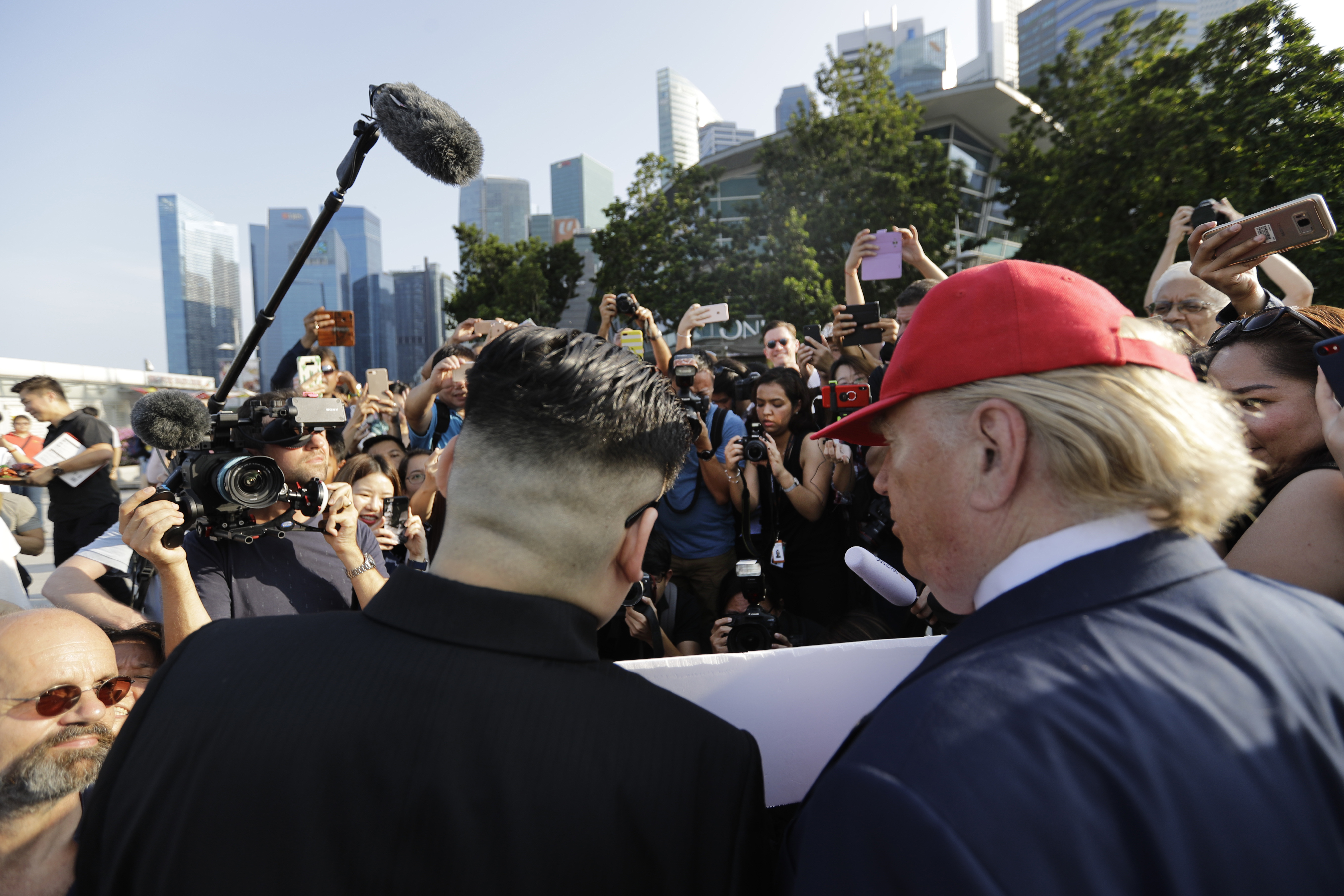 In this June 8, 2018, photo, Kim Jong Un and Donald Trump impersonators, are swamped by members of the media and curious onlookers as they visited the Merlion Park, a popular tourist destination in Singapore. The small island nation of Singapore, which prides itself on law and order, is feeling the pressure of more than 3,000 members of the press arriving for a historic summit between President Donald Trump and North Korean leader Kim Jong Un. Apart from journalists, authorities also have to contend with Kim and Trump impersonators. (AP Photo/Wong Maye-E)