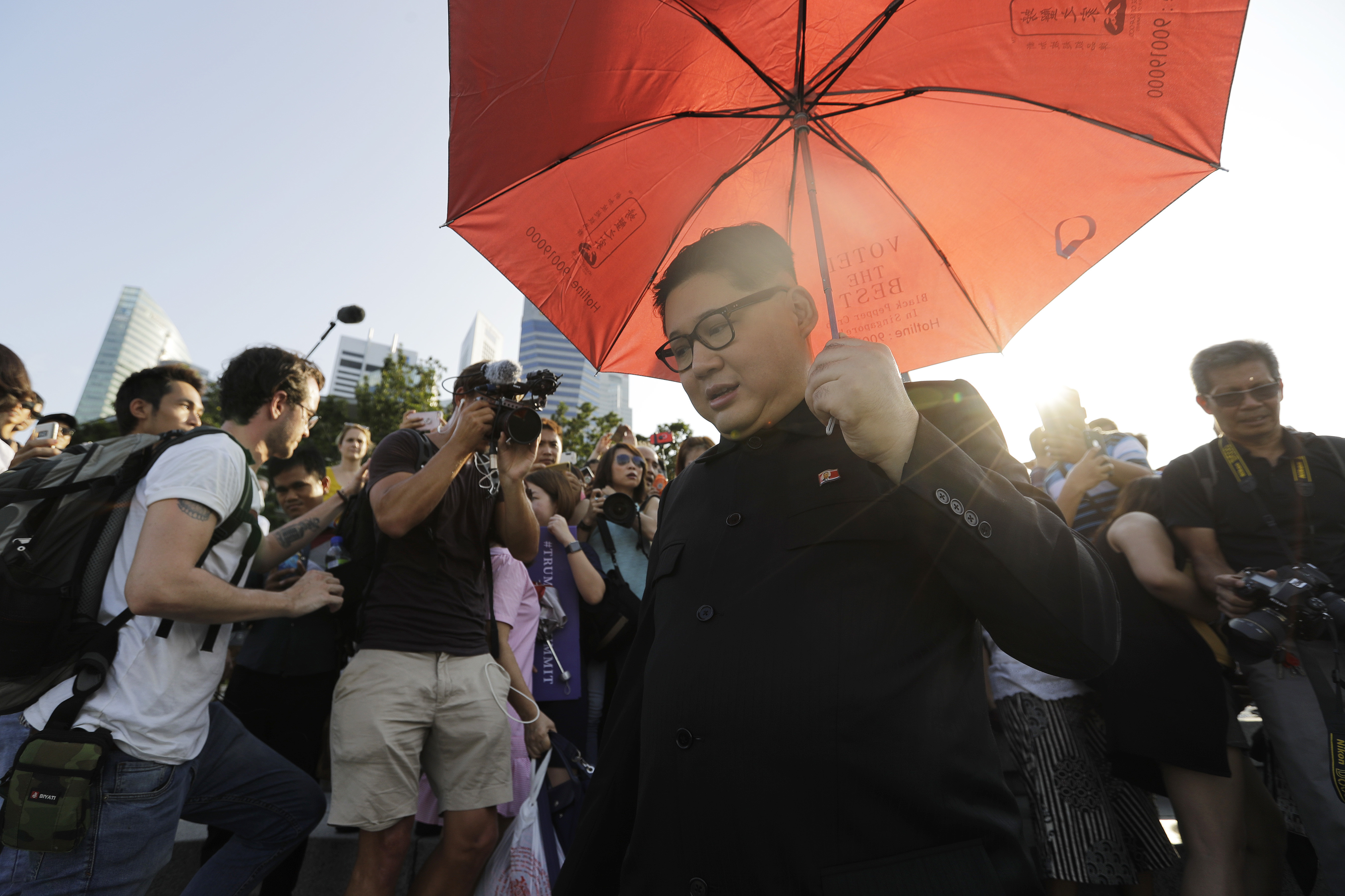 In this June 8, 2018, photo, Kim Jong Un impersonator, Howard X, who was questioned by police when he arrived at Singapore's Changi Airport is swamped by members of the media and curious onlookers as he visited the Merlion Park, a popular tourist destination in Singapore. The small island nation of Singapore, which prides itself on law and order, is feeling the pressure of more than 3,000 members of the press arriving for a historic summit between President Donald Trump and North Korean leader Kim Jong Un. Apart from journalists, authorities also have to contend with Kim and Trump impersonators. (AP Photo/Wong Maye-E)