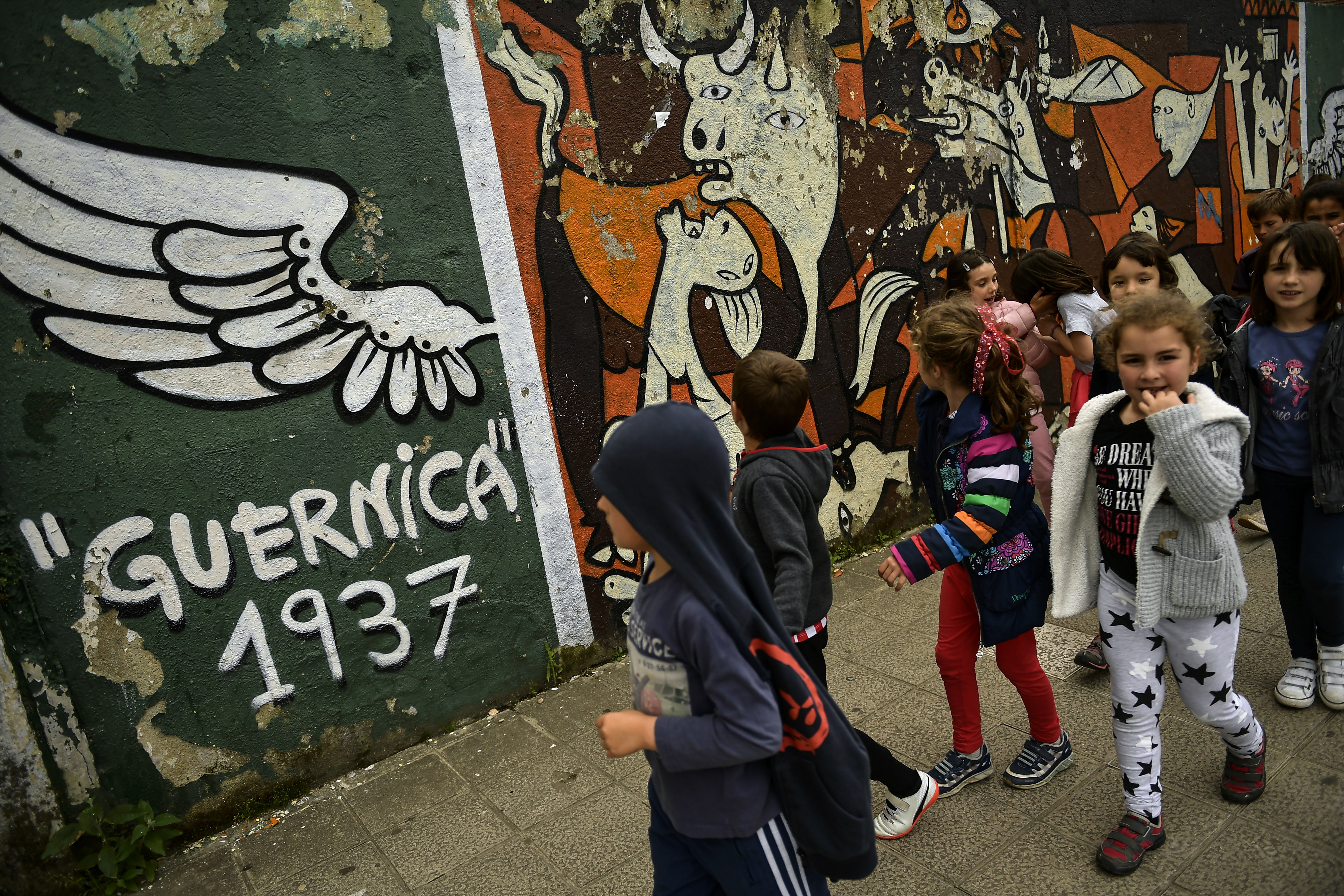 A group of young girls and boys walk past a wall with the Pablo Picasso's painting in tribute for all people killed in the Spanish Civil War, in Guernica, northern Spain, Thursday, April 26, 2018. The small town was destroyed in an attack by German bombers and thousands of Basque citizens died on this day in 1937. The carnage has ever since stood as a symbol of man's cruelty to his fellow man, immortalized in Pablo Picasso's immense and powerful painting, one of the most iconic works of art of the 20th century. (AP Photo/Alvaro Barrientos)