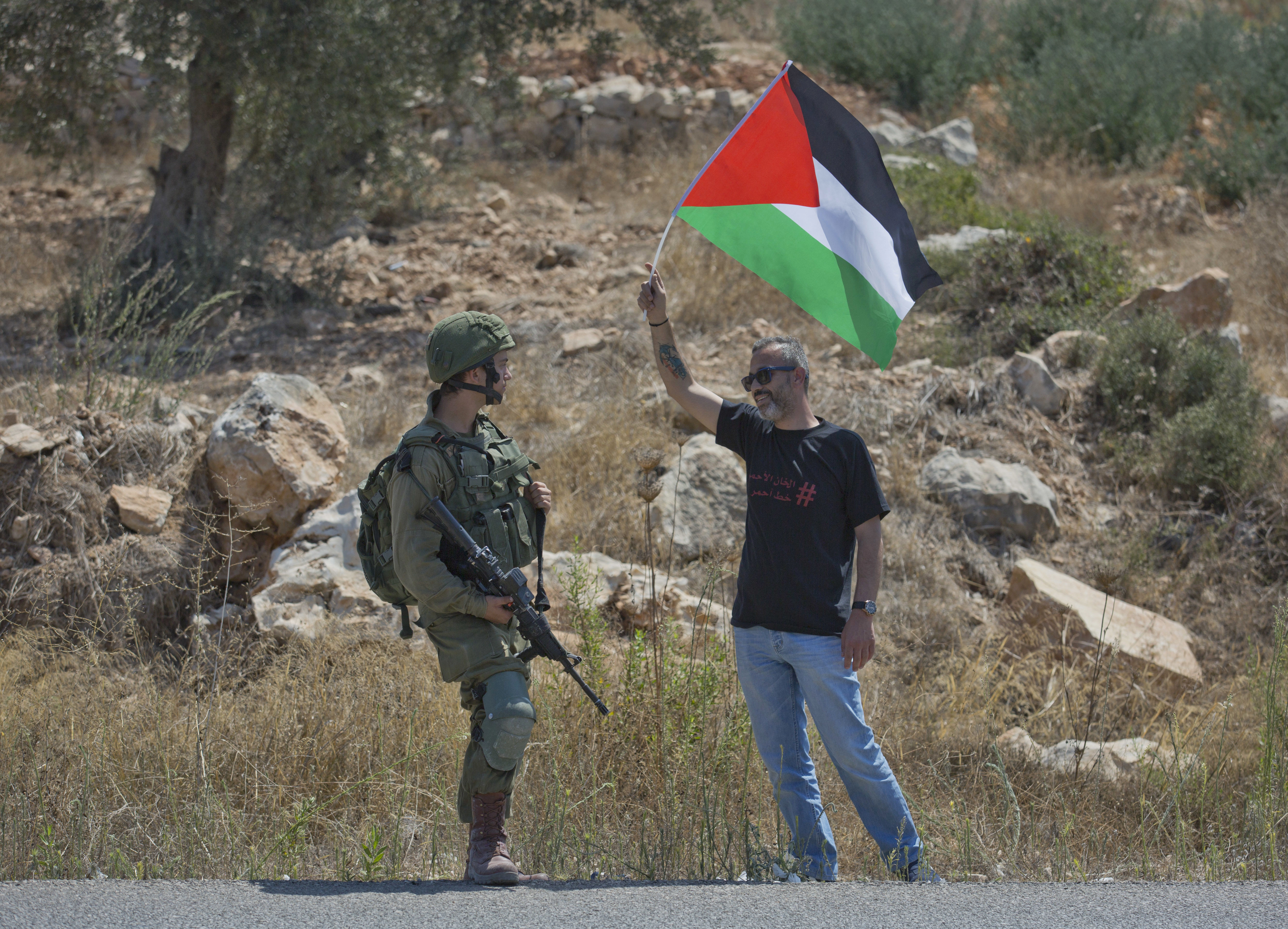 A protester flies a Palestinian flag in front of an Israeli soldier while army excavators and bulldozers continue, for the second day, to work at the lands of the West Bank village of Ras Karkar, near Ramallah, Wednesday, Aug. 29, 2018. (AP Photo/Nasser Nasser)