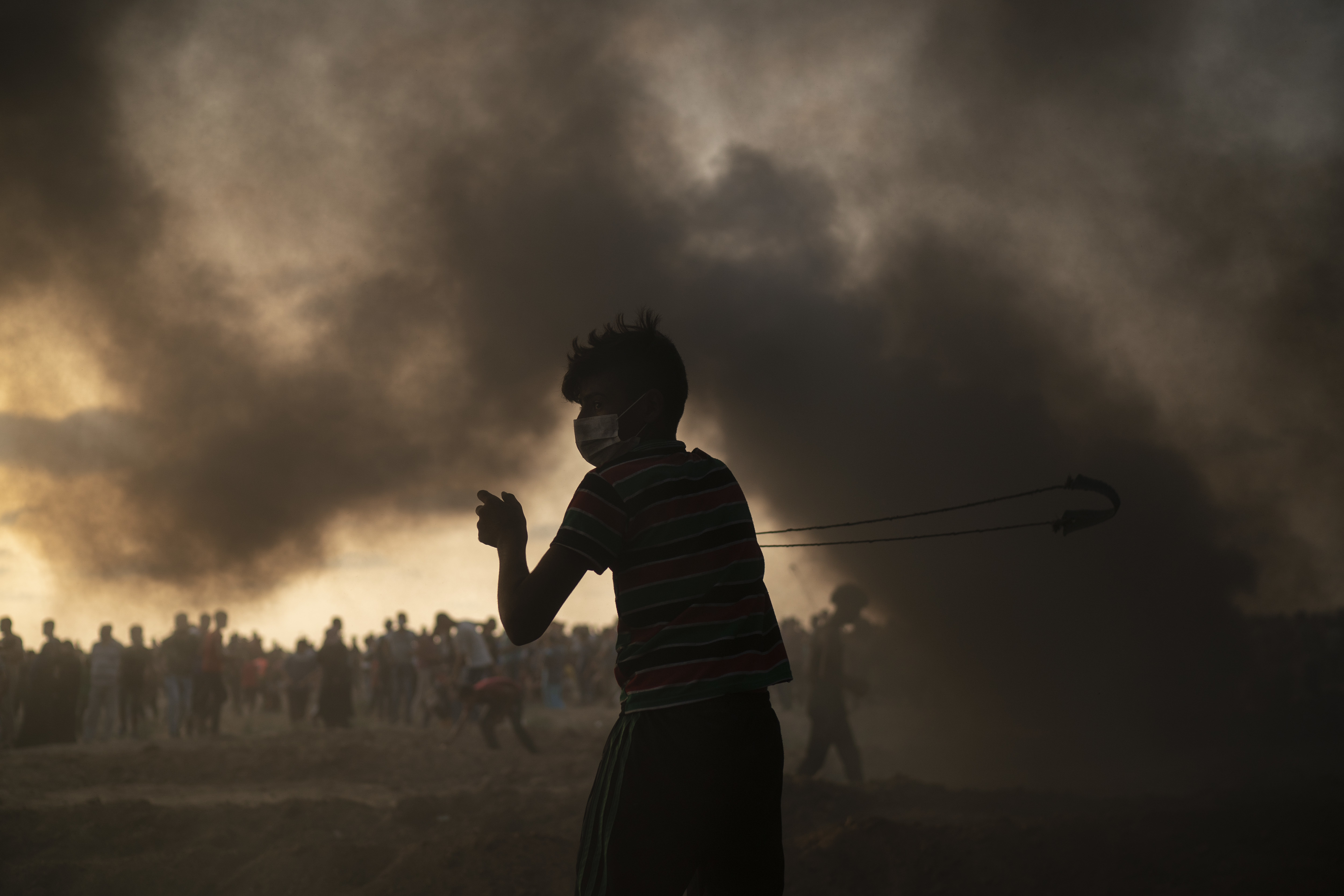 A young protester hurls stones while others burn tires during a protest at Gaza Strip's border with Israel, east of Gaza City, Friday, Aug. 31, 2018. Gaza's Health Ministry says Israeli gunfire wounded about 80 Palestinians at a weekly protest along the border with Israel. (AP Photo/Felipe Dana)