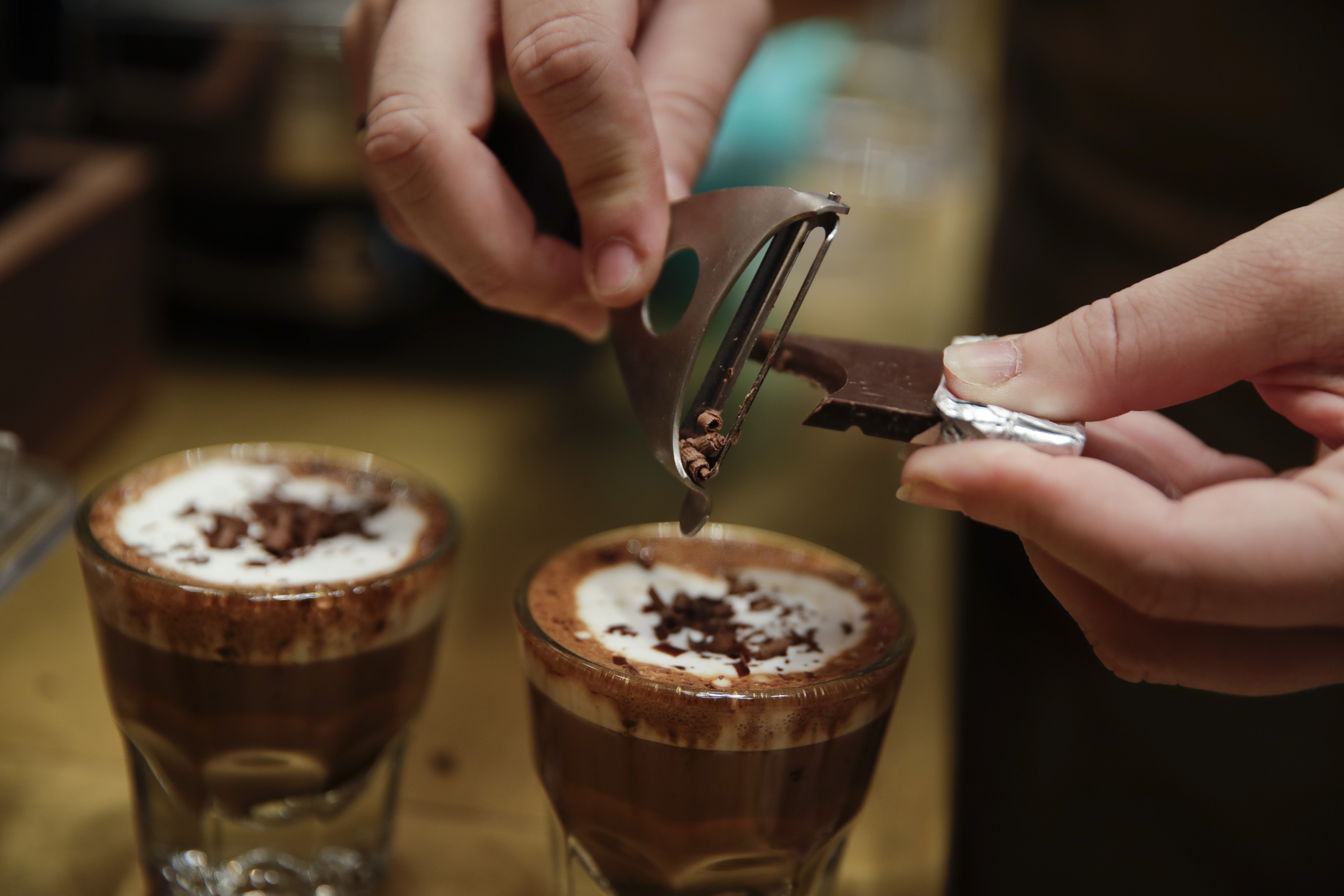 In this photo taken on Tuesday, Sept. 4, 2108, a waiter adds chocolate to coffee cups, at the Starbucks store in Milan, Italy. Starbucks opens its first store in Italy Friday, betting that premium brews and novelties like a heated marble-topped coffee bar will win patrons in a country fond of its espresso rituals. Decades ago, Milan’s coffee bars had inspired the chain’s vision. Starbucks hopes clients will linger at Starbucks Reserve Roastery, where they can watch beans being roasted, sip Reserve coffee or have cocktails at a mezzanine-level bar in a cavernous space that once was a post office near the city’s Duomo, or cathedral. (AP Photo/Luca Bruno)