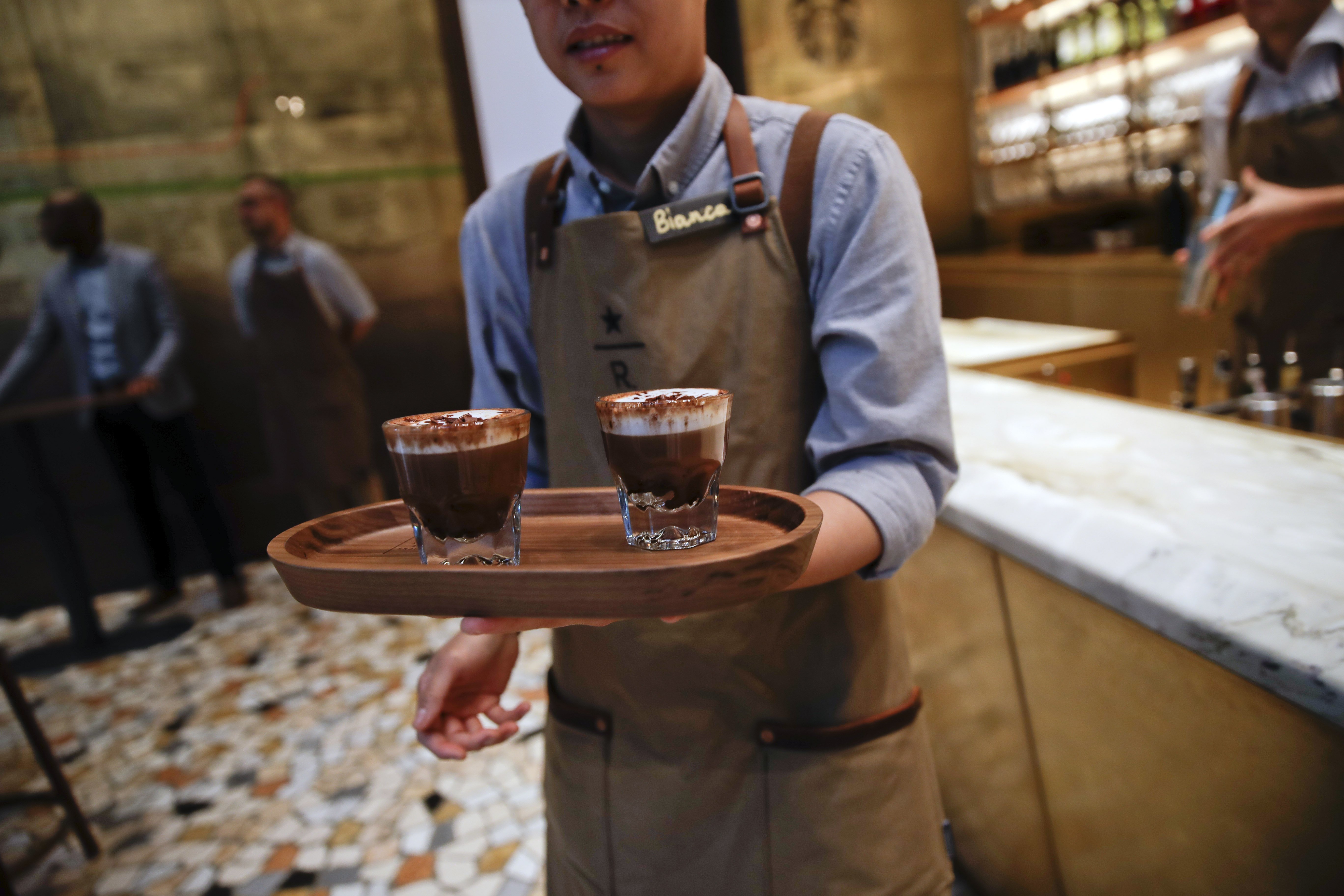 In this photo taken on Tuesday, Sept. 4, 2108, a waiter serves cappuccini at the Starbucks store in Milan, Italy. Starbucks opens its first store in Italy Friday, betting that premium brews and novelties like a heated marble-topped coffee bar will win patrons in a country fond of its espresso rituals. Decades ago, Milan’s coffee bars had inspired the chain’s vision. Starbucks hopes clients will linger at Starbucks Reserve Roastery, where they can watch beans being roasted, sip Reserve coffee or have cocktails at a mezzanine-level bar in a cavernous space that once was a post office near the city’s Duomo, or cathedral. (AP Photo/Luca Bruno)