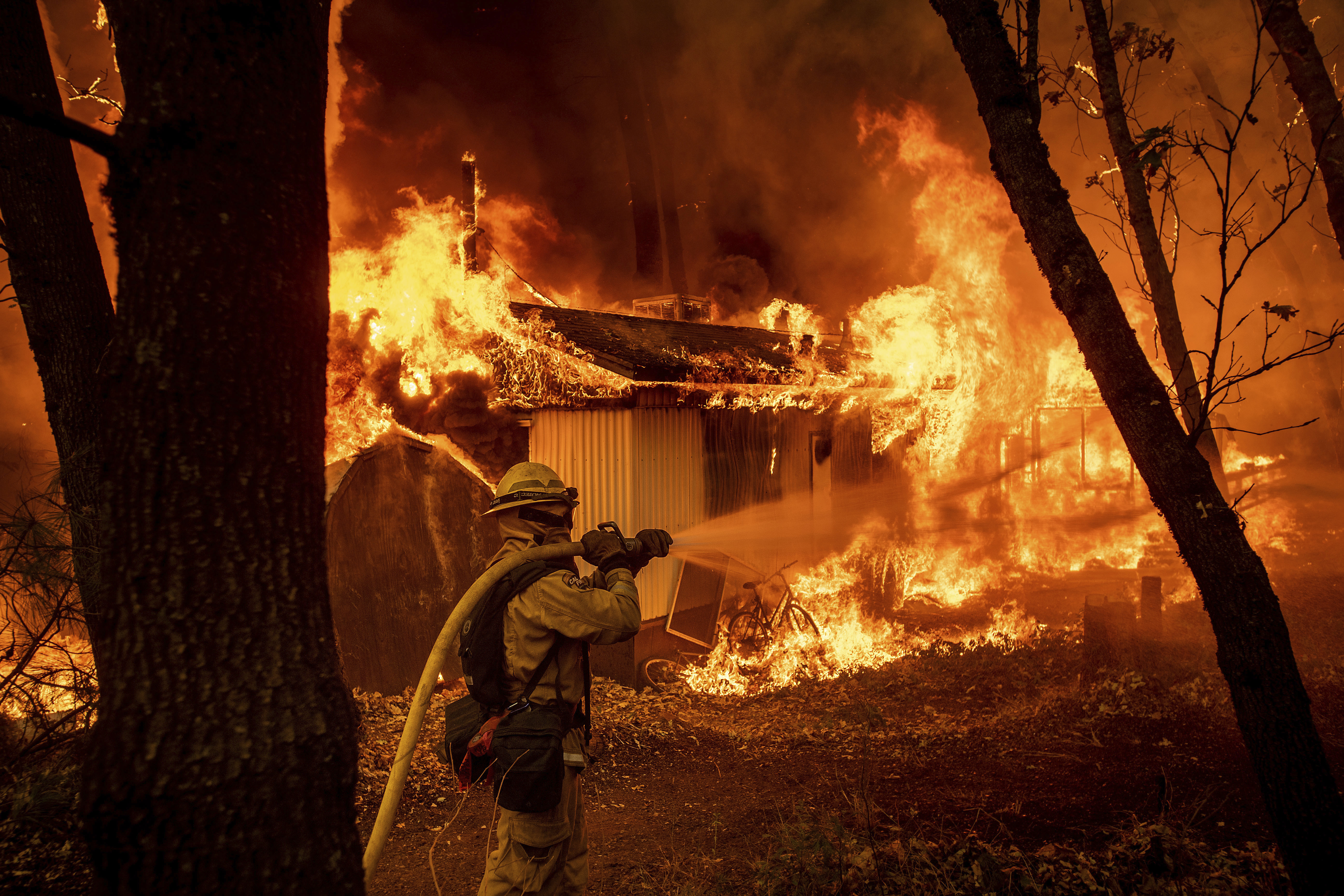 Firefighter Jose Corona sprays water as flames from the Camp Fire consume a home in Magalia, Calif., on Friday, Nov. 9, 2018. (AP Photo/Noah Berger)