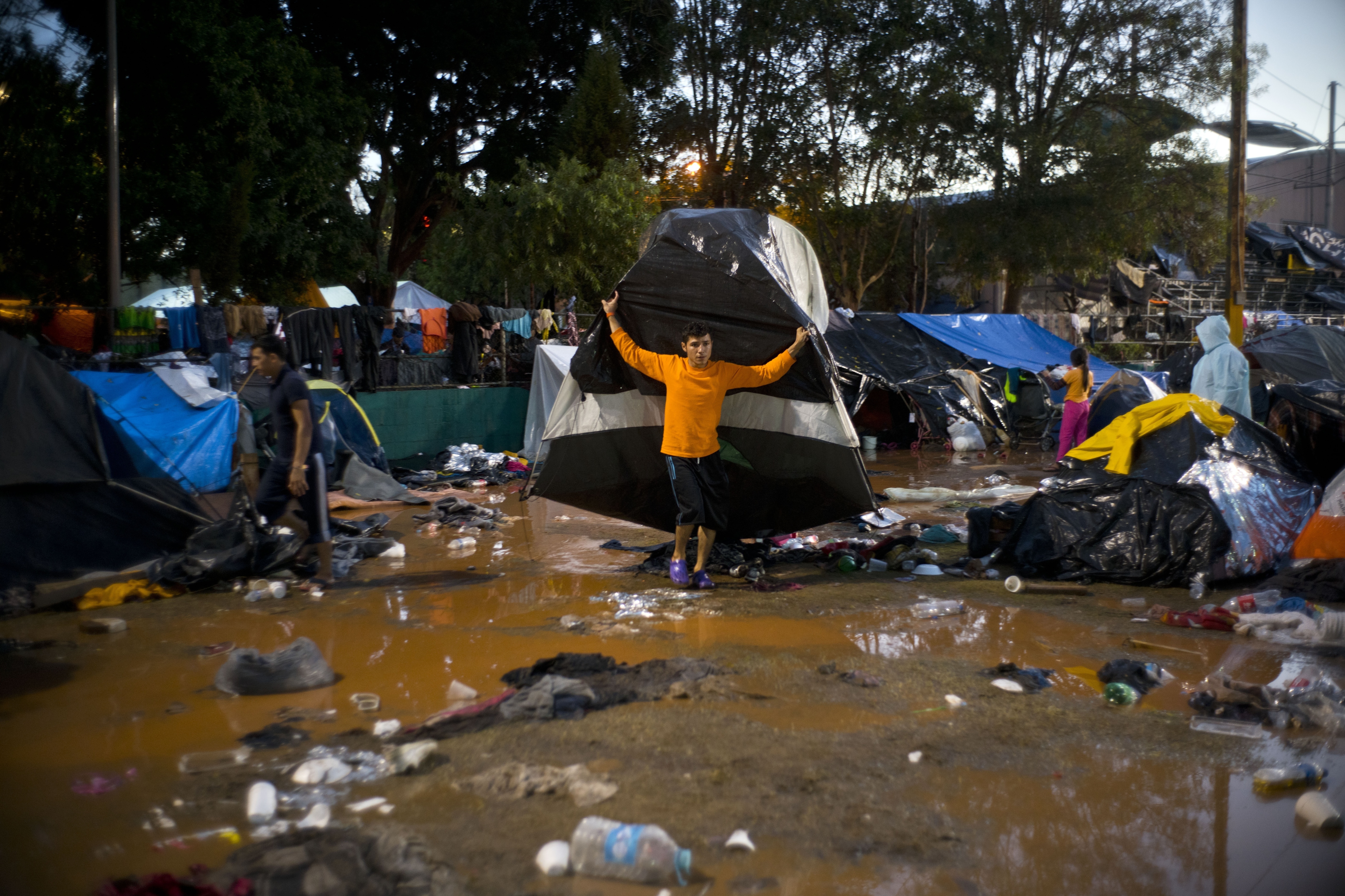 A migrant moves his tent in the rain before he was being transferred by bus to another shelter in better conditions than the flooded sports complex where thousands of Central Americans were living, in Tijuana, Mexico, following heavy rains, on Thursday, Nov. 29, 2018. Aid workers and humanitarian organizations expressed concerns Thursday about the unsanitary conditions at the sports complex in Tijuana where more than 6,000 Central American migrants are packed into a space adequate for half that many people and where lice infestations and respiratory infections are rampant. (AP Photo/Ramon Espinosa)