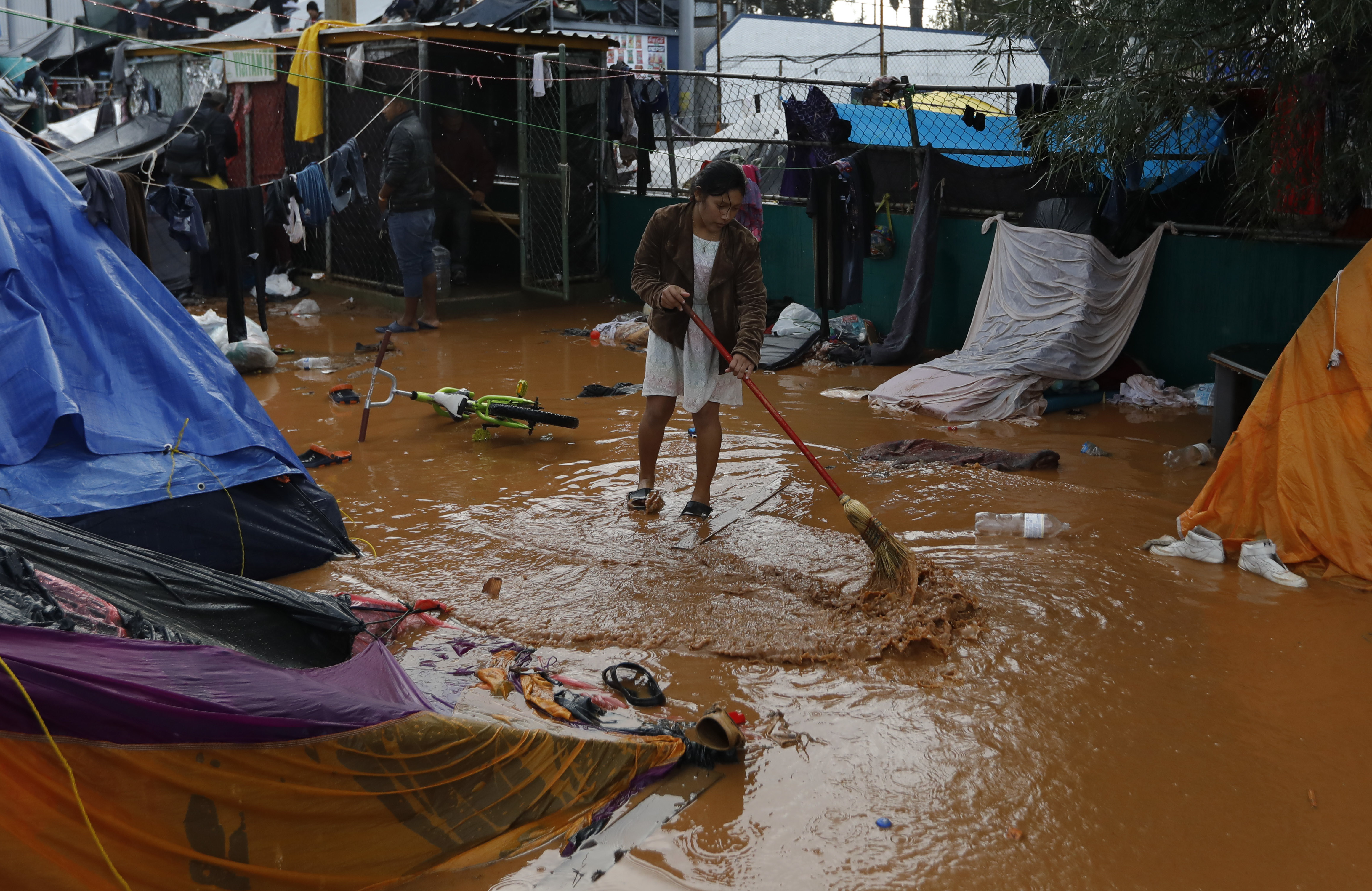 A woman attempts to sweep away flood waters, between bouts of heavy rain at a sports complex sheltering thousands of Central Americans in Tijuana, Mexico, Thursday, Nov. 29, 2018. Aid workers and humanitarian organizations expressed concerns Thursday about the unsanitary conditions at the sports complex in Tijuana where more than 6,000 Central American migrants are packed into a space adequate for half that many people and where lice infestations and respiratory infections are rampant.(AP Photo/Rebecca Blackwell)