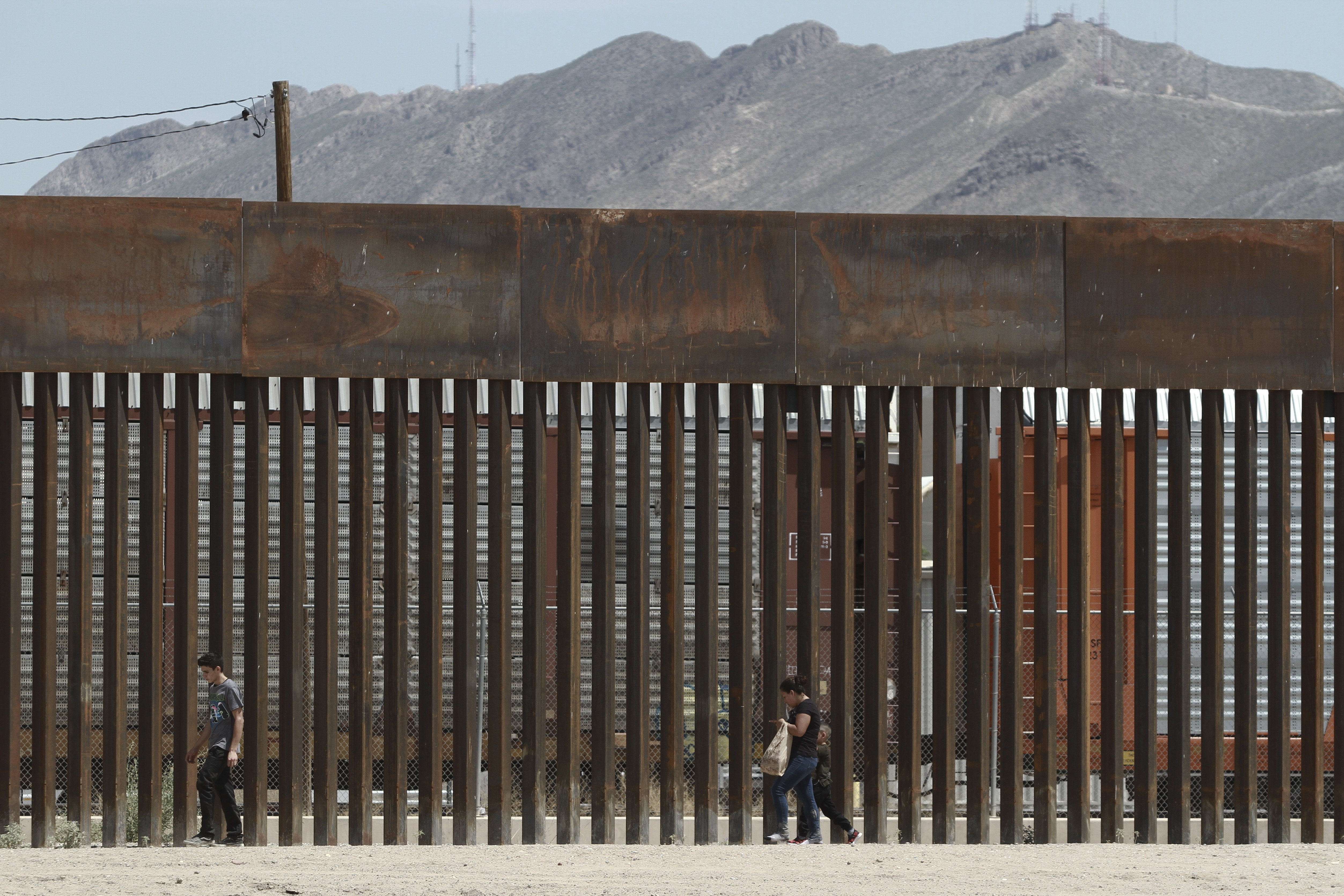 Three migrants who had managed to evade the Mexican National Guard and cross the Rio Grande onto U.S. territory walk along a border wall set back from the geographical border, in El Paso, Texas, as seen from Ciudad Juarez, Mexico, Wednesday, July 17, 2019. Border Patrol agents opened a door in the wall to escort them into a waiting patrol car. It was not clear whether the migrants, already on U.S. soil, would still be able to submit a claim for asylum under a new U.S. policy that went into effect Tuesday.(AP Photo/Christian Chavez)