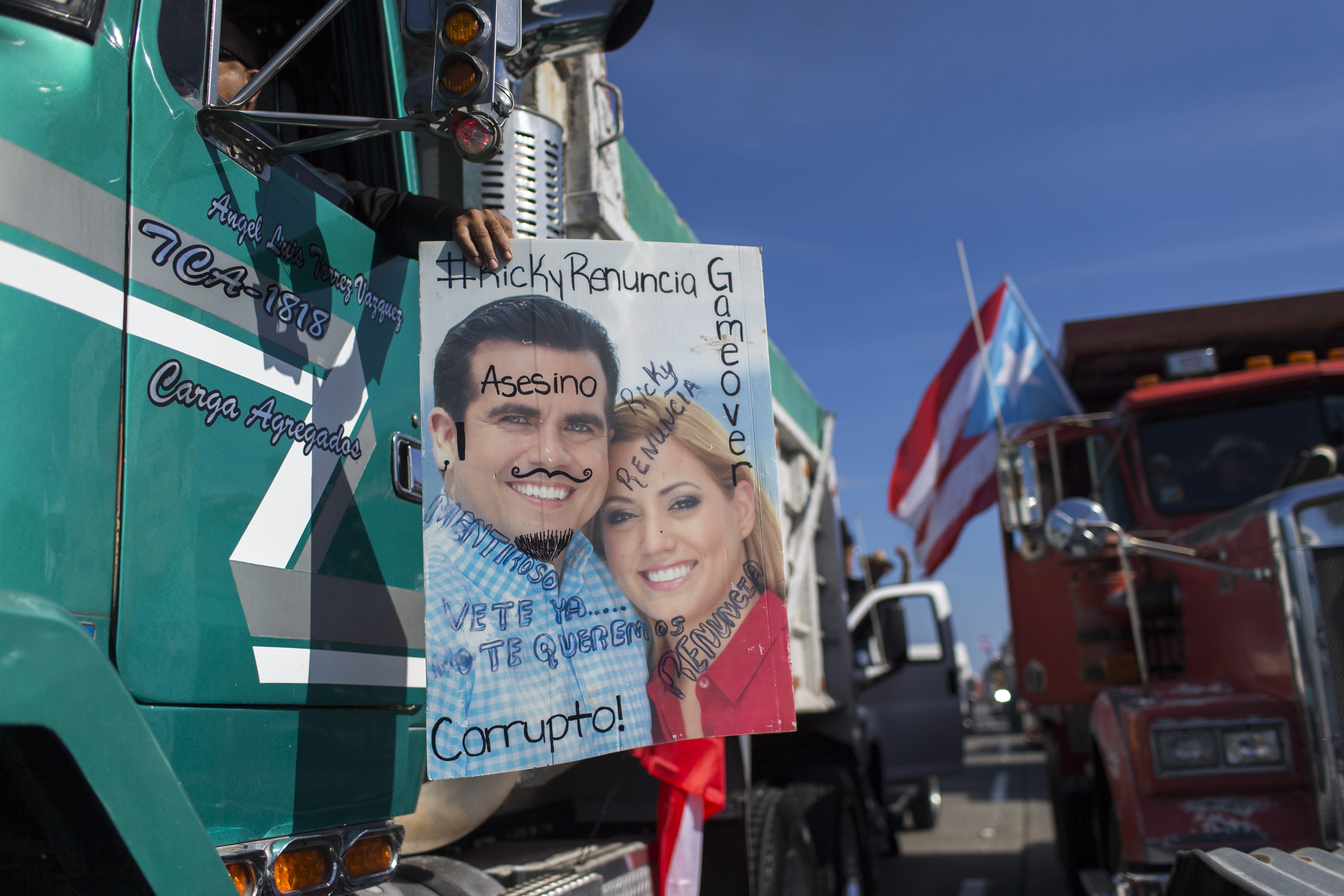 Demonstrators carry a defaced poster of Governor Ricardo Rossello and his wife, with inscriptions that read in Spanish 