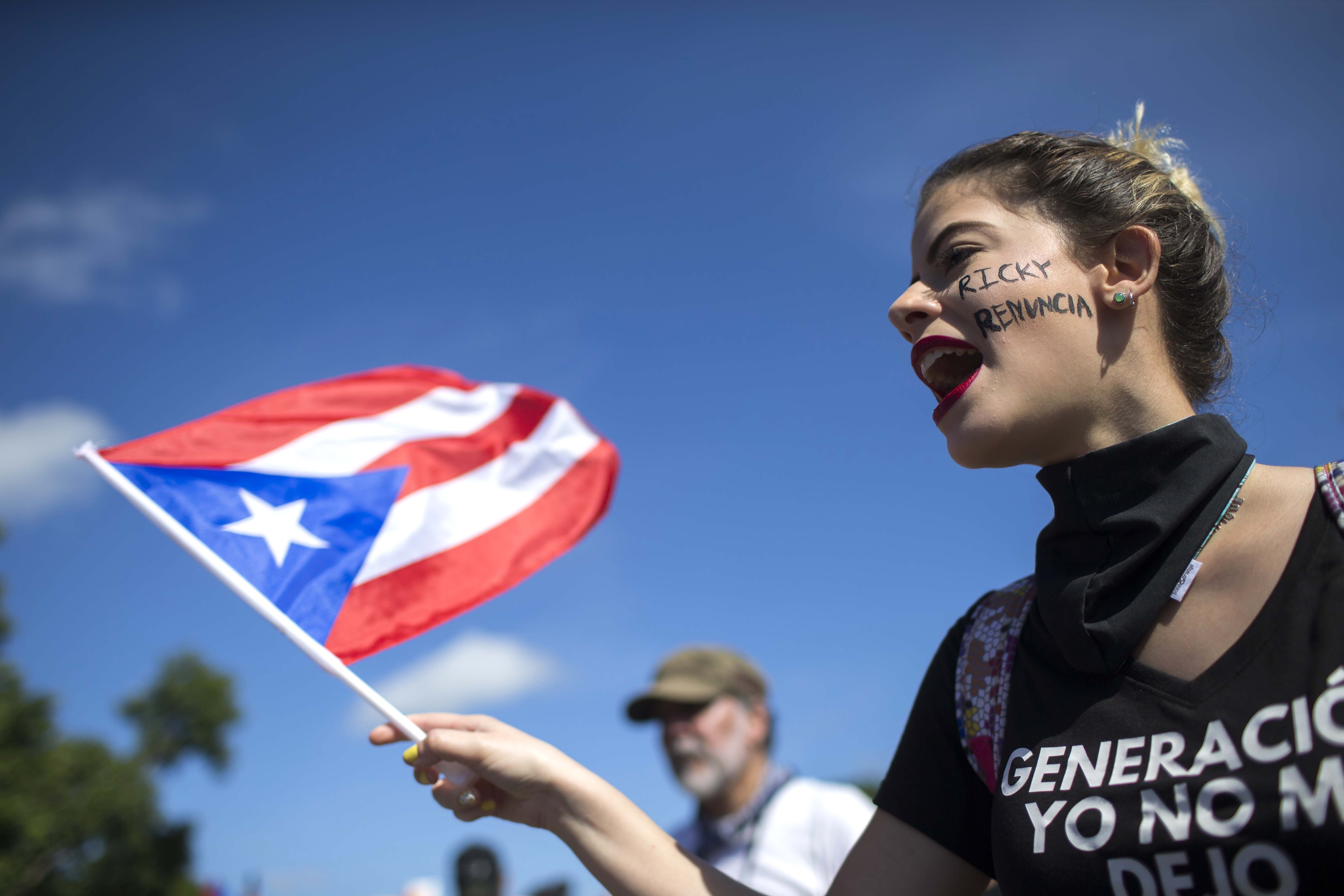 A woman flies a Puerto Rico flag during a protest to demand the resignation of Governor Ricardo Rossello from office, in San Juan, Puerto Rico, Monday, July 22, 2019. Protesters are demanding Rossello step down for his involvement in a private chat in which he used profanities to describe an ex-New York City councilwoman and a federal control board overseeing the island's finance. (AP Photo/Dennis M. Rivera Pichardo)