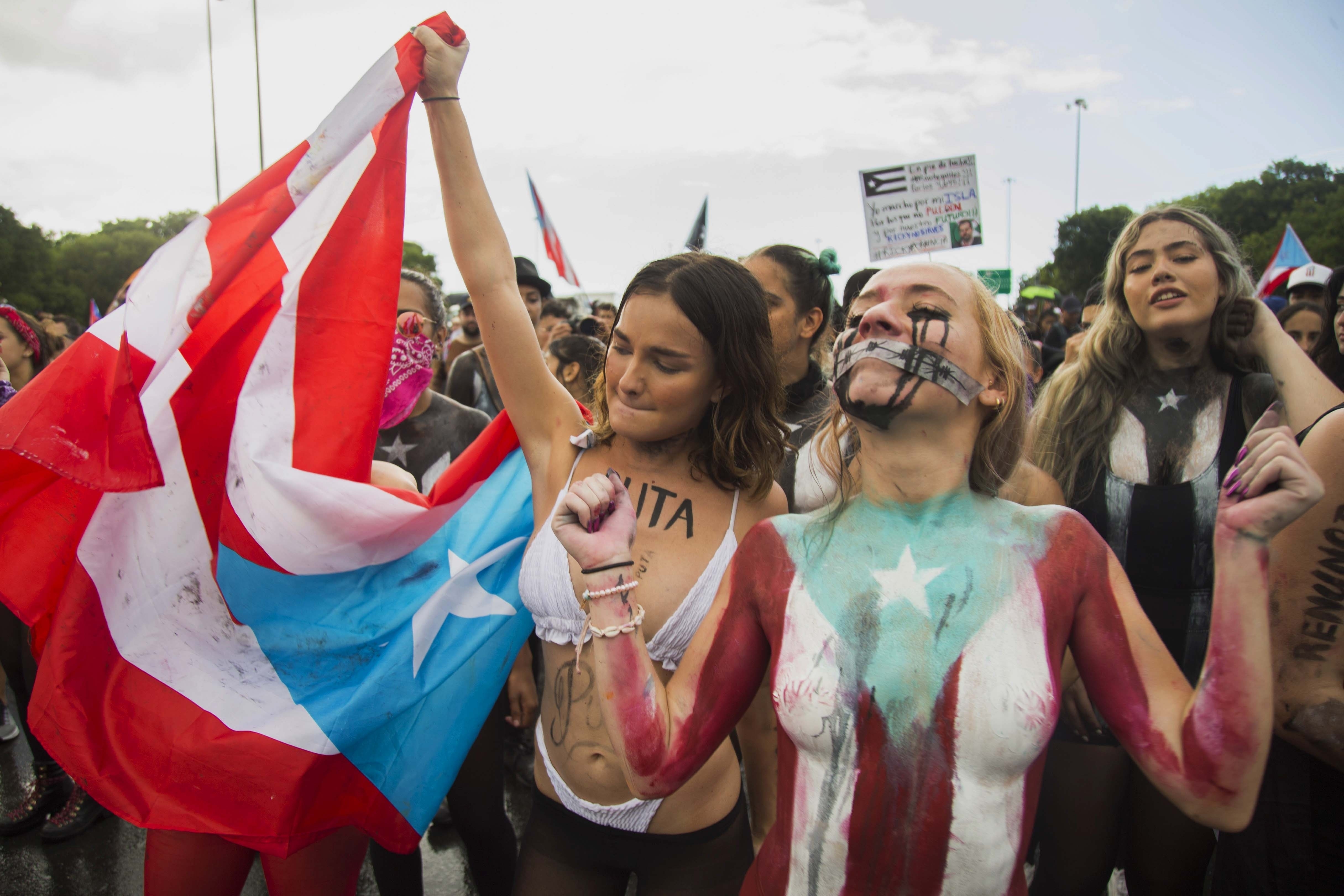 Young women join a protest to demand the resignation of Governor Ricardo Rossello from office, in San Juan, Puerto Rico, Monday, July 22, 2019. Protesters are demanding Rossello step down for his involvement in a private chat in which he used profanities to describe an ex-New York City councilwoman and a federal control board overseeing the island's finance. (AP Photo/Dennis M. Rivera Pichardo)