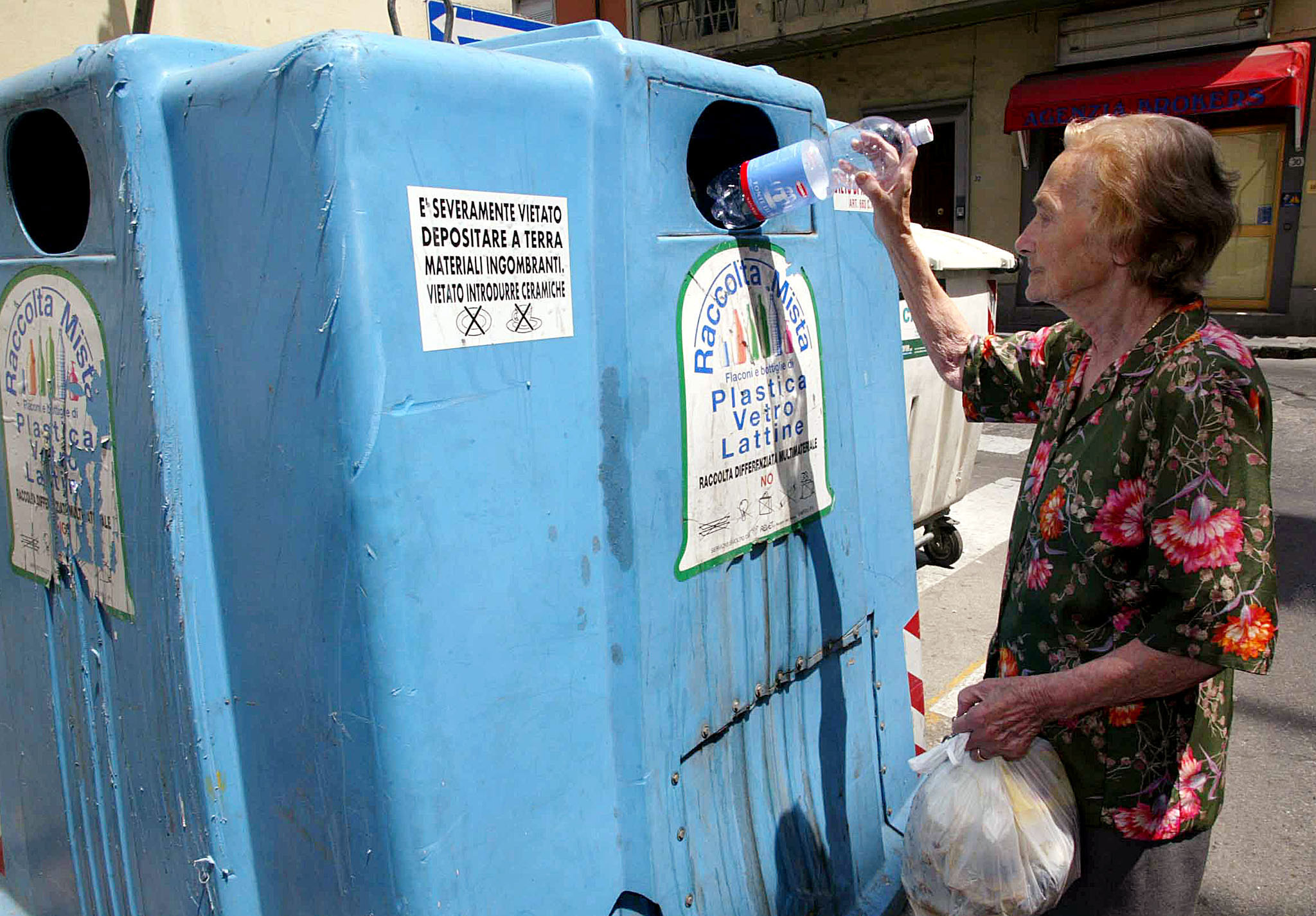 Un'anziana signora getta una bottiglia di plastica nel contenitore della raccolta differenziata
