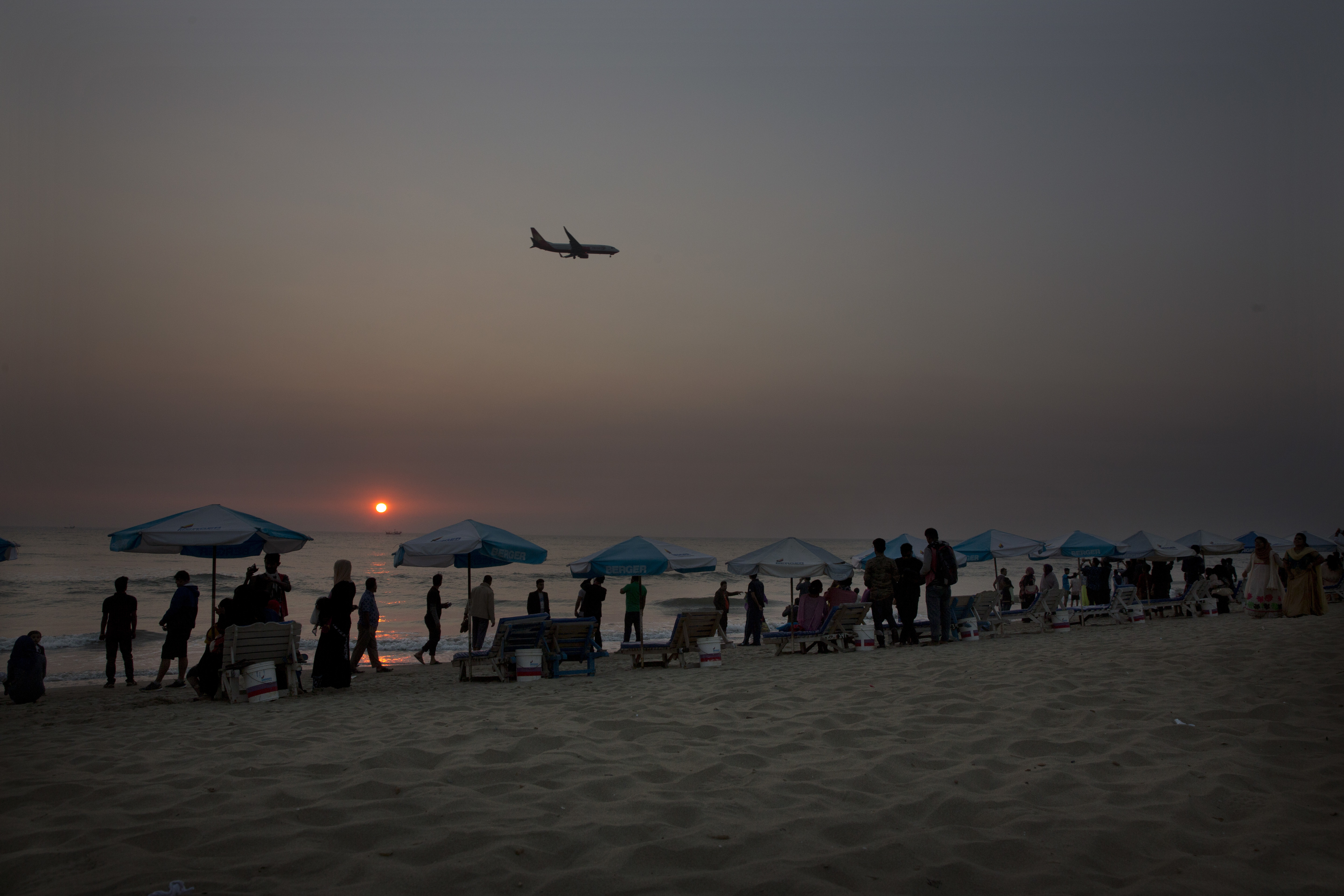 Bangladeshis enjoy sunset at a beach as an aeroplanes flies past in Cox's Bazar, Bangladesh Friday, Jan. 26, 2018. Miles-long beaches makes this coastal district Bangladesh's top tourist destination. (AP Photo/Manish Swarup)