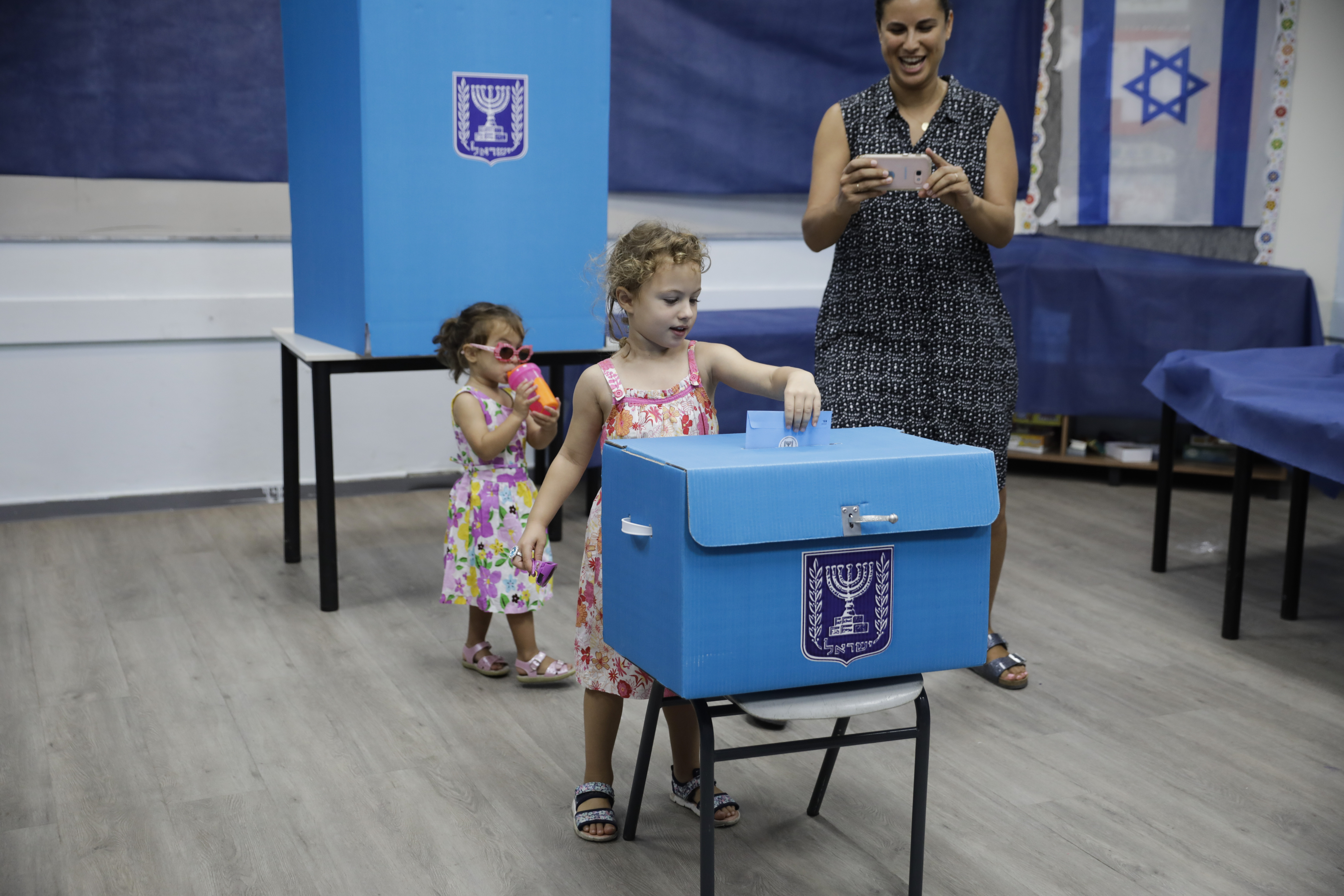 A woman takes a photo of her daughter at a poling station in Rosh Haayin, Israel, Tuesday, Sept. 17, 2019. Israelis began voting Tuesday in an unprecedented repeat election that will decide whether longtime Prime Minister Benjamin Netanyahu stays in power despite a looming indictment on corruption charges. (AP Photo/Sebastian Scheiner)