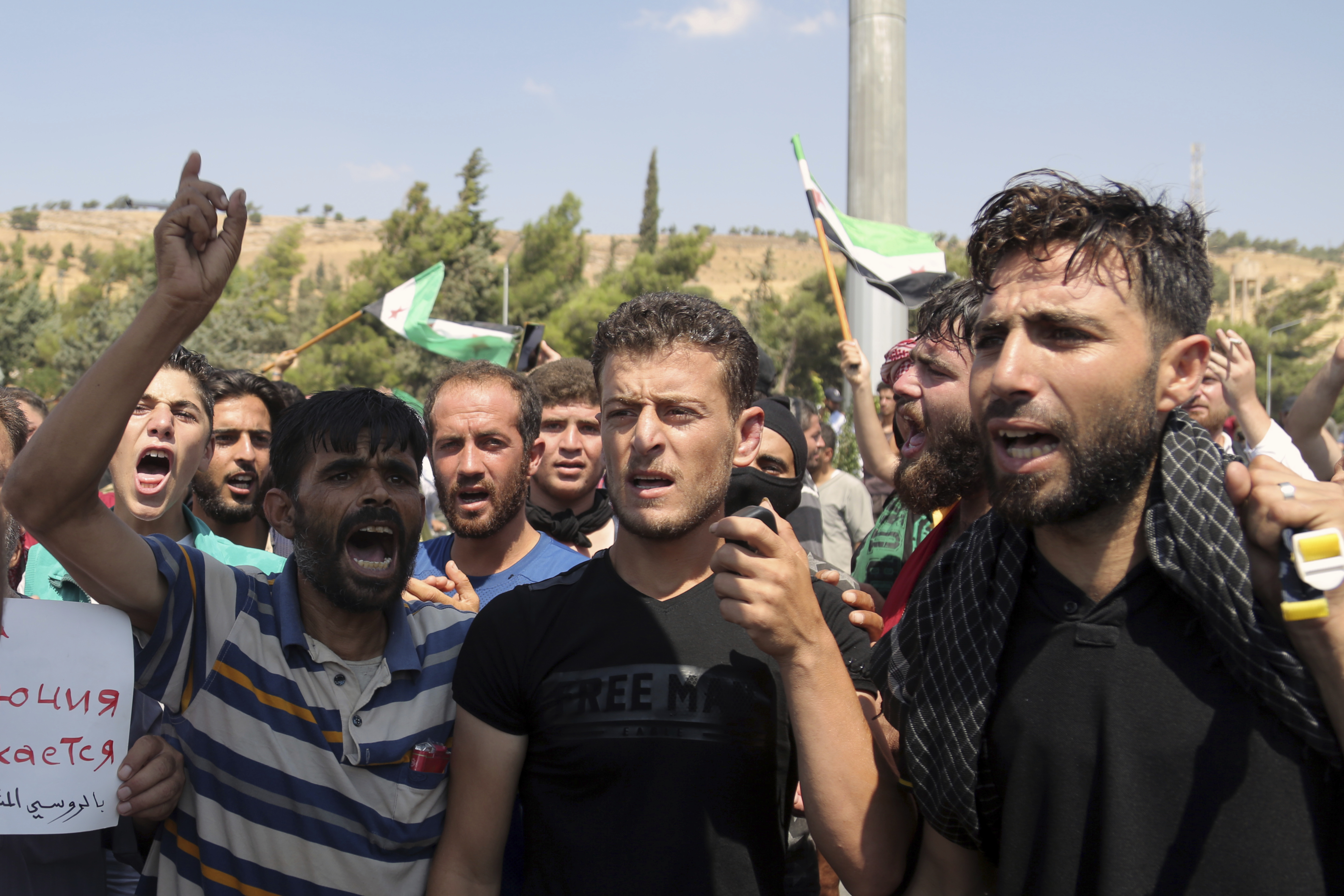 Protesters chant slogans as they hold Syrian revolutionary flags during a demonstration at the Bab al-Hawa border crossing with Turkey, Syria, Friday, Aug. 30, 2019, demanding that Ankara either open the border or end attacks by the government. Opposition activists said Turkish borders guards fired tear gas at the protesters. (AP Photo)