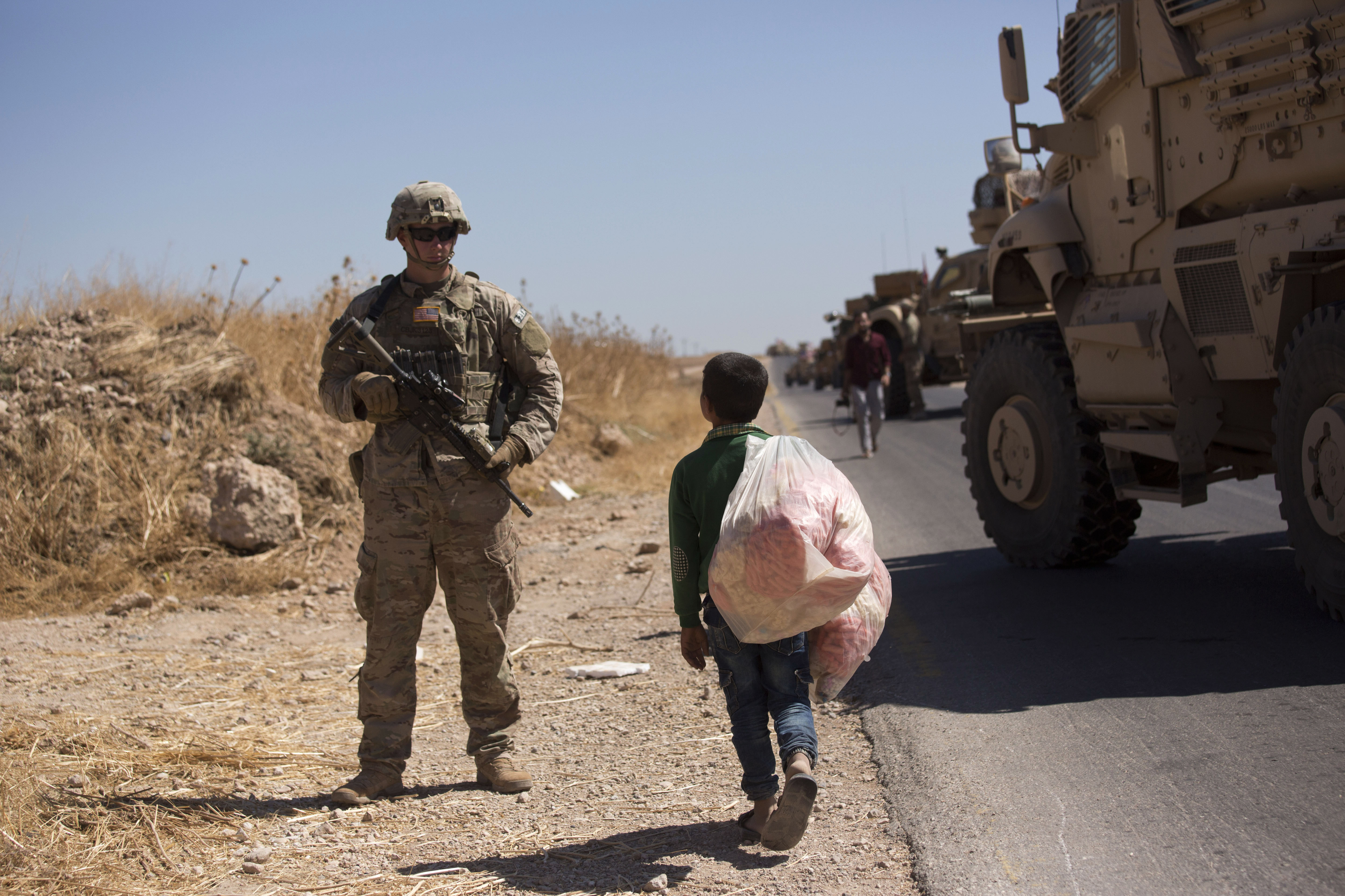 A Syrian boy selling snacks looks at a U.S. soldier standing guard during the first joint ground patrol by American and Turkish forces in the so-called 
