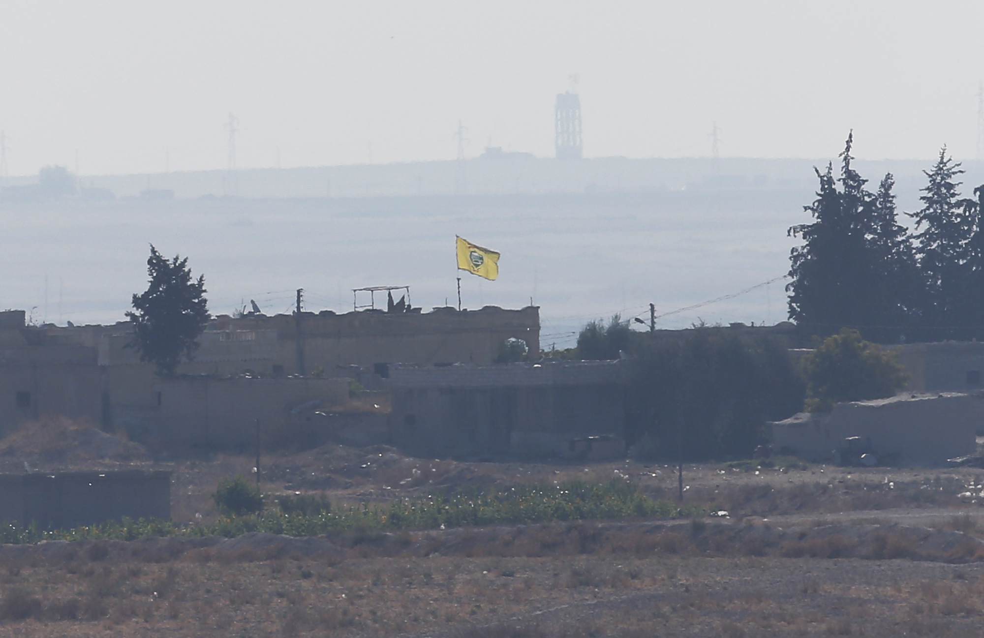 In this photo taken from the Turkish side of the border between Turkey and Syria, in Akcakale, Sanliurfa province, southeastern Turkey, a flag of Kurdish People's Protection Units, or YPG, flies on a building in the Syrian town of Tel Abyad, Tuesday, Oct. 8, 2019.  Turkey's vice president says his country won't bow to threats in an apparent response to U.S. President Donald Trump's warning to Ankara about the scope of its planned military incursion into Syria aiming to create a zone that would allow Turkey to resettle Syrian refugees there. (AP Photo/Lefteris Pitarakis)