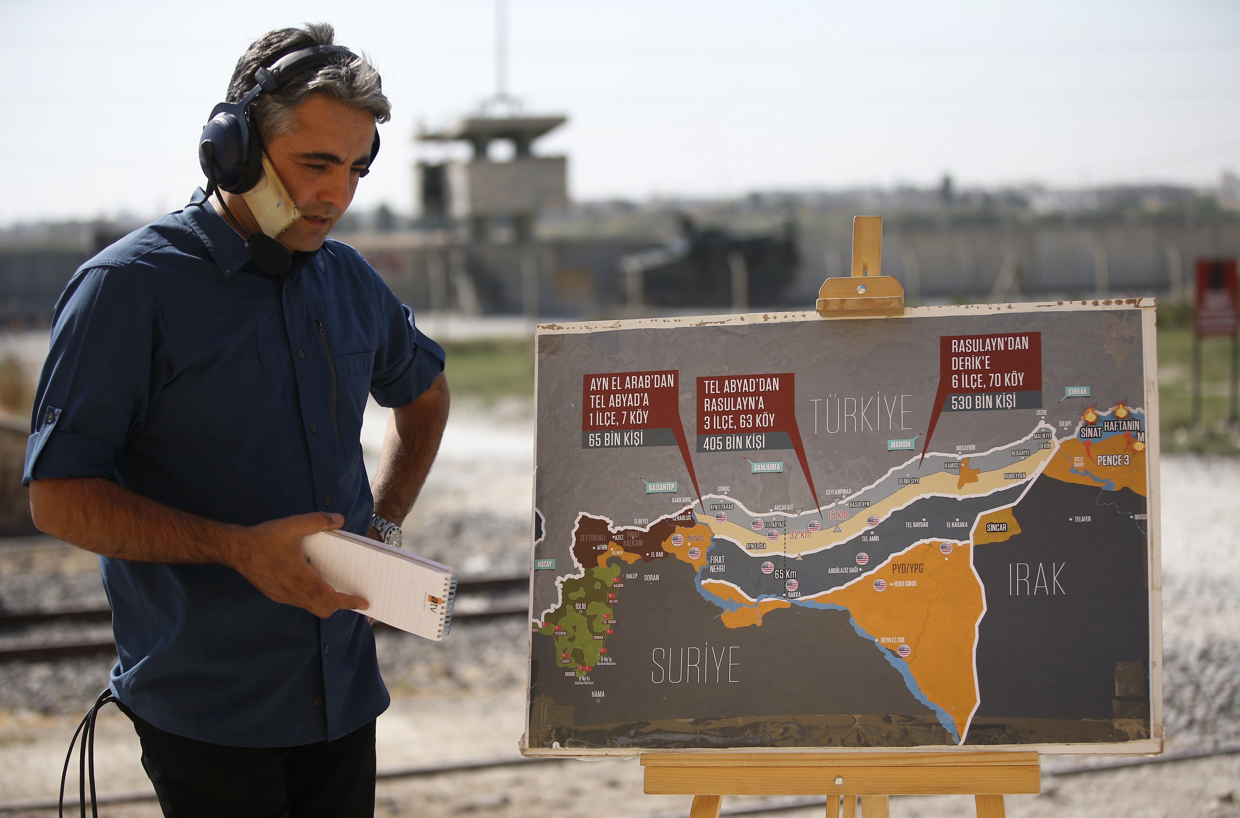 A TV journalist prepares to work in front of a map showing Turkey's suggested operation in Syria, at the border between Turkey and Syria, in Akcakale, Sanliurfa province, southeastern Turkey, Tuesday, Oct. 8, 2019. Turkey's vice president Fuat Oktay says his country won't bow to threats in an apparent response to U.S. President Donald Trump's warning to Ankara about the scope of its planned military incursion into Syria. (AP Photo/Lefteris Pitarakis)