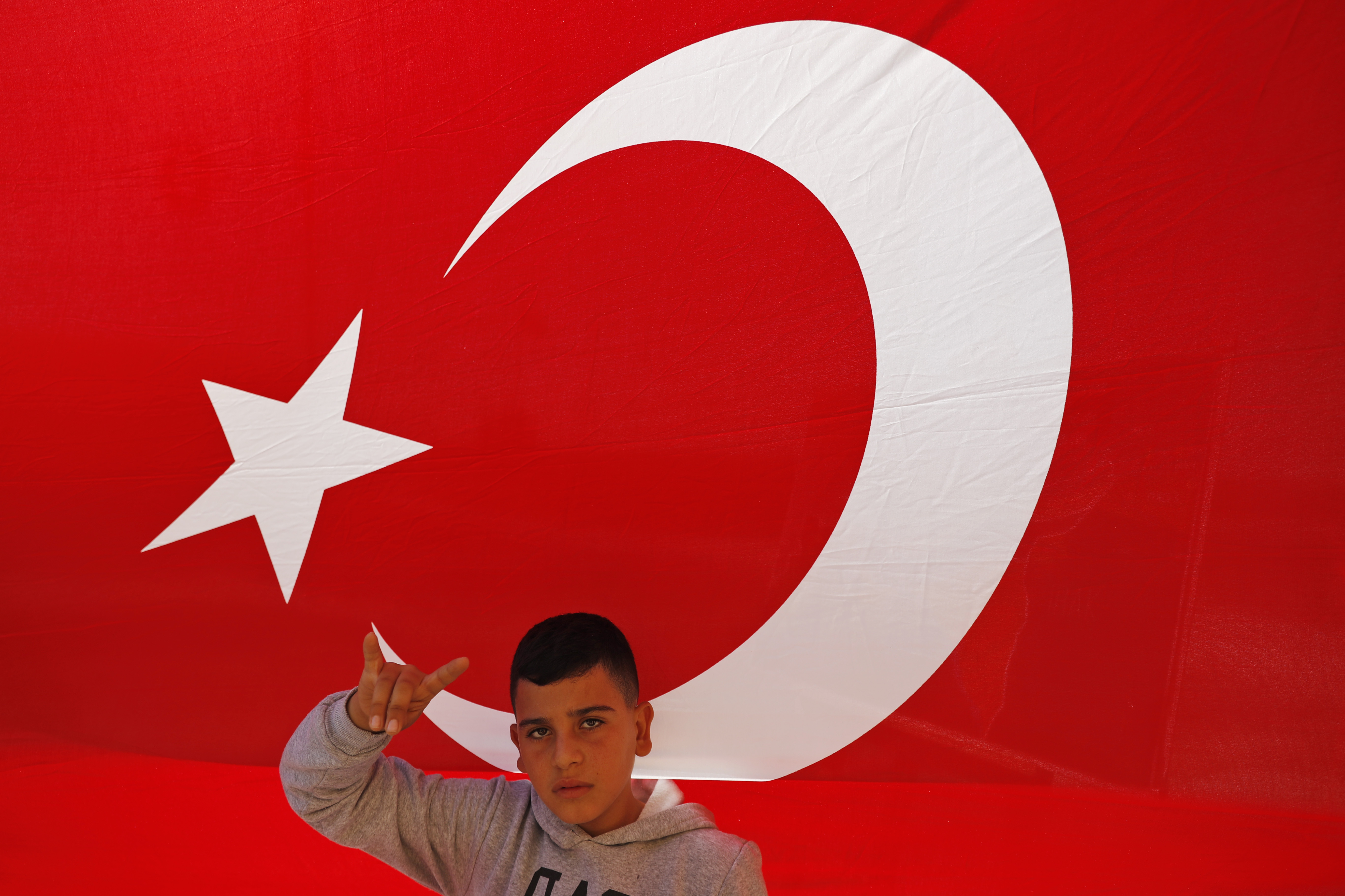 A youth flashes a hand gesture representing the Turkish far-right gray wolves organisation as he stands by a flag of Turkey's Nationalist Movement Party (MHP) at the Turkish side of the border between Turkey and Syria, in Akcakale, Sanliurfa province, southeastern Turkey, Tuesday, Oct. 8, 2019. Turkey's vice president Fuat Oktay says his country won't bow to threats in an apparent response to U.S. President Donald Trump's warning to Ankara about the scope of its planned military incursion into Syria. (AP Photo/Lefteris Pitarakis)