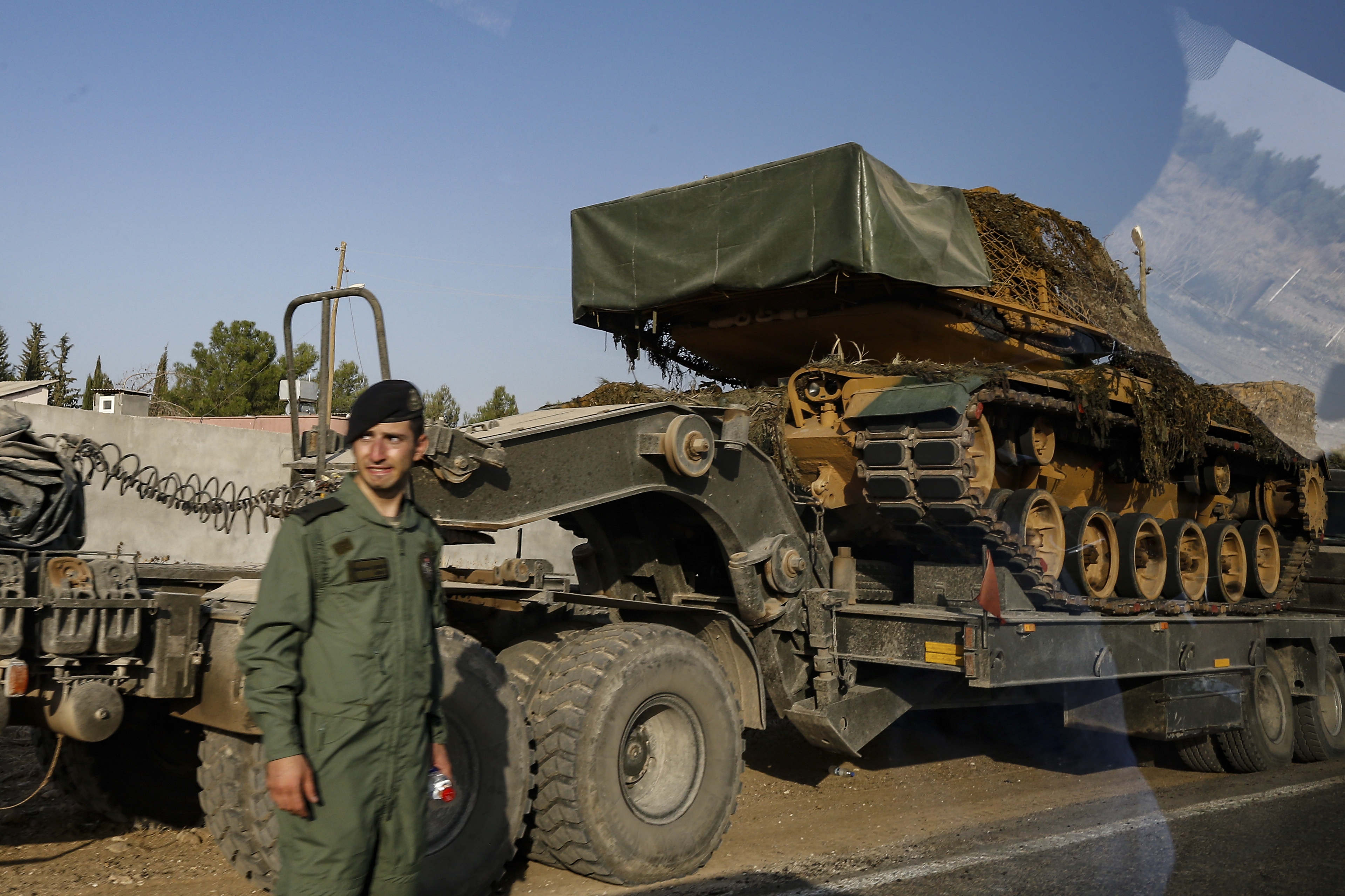 A Turkish forces soldiers looks on as tanks are transported by trucks to their new positions on a road towards the border with Syria in Sanliurfa province, Turkey, on Monday, Oct. 14, 2019. Syrian troops entered several northern towns and villages Monday, getting close to the Turkish border as Turkey's army and opposition forces backed by Ankara marched south in the same direction, raising concerns of a clash between the two sides as Turkey's invasion of northern Syria entered its sixth day. (AP Photo/Emrah Gurel)