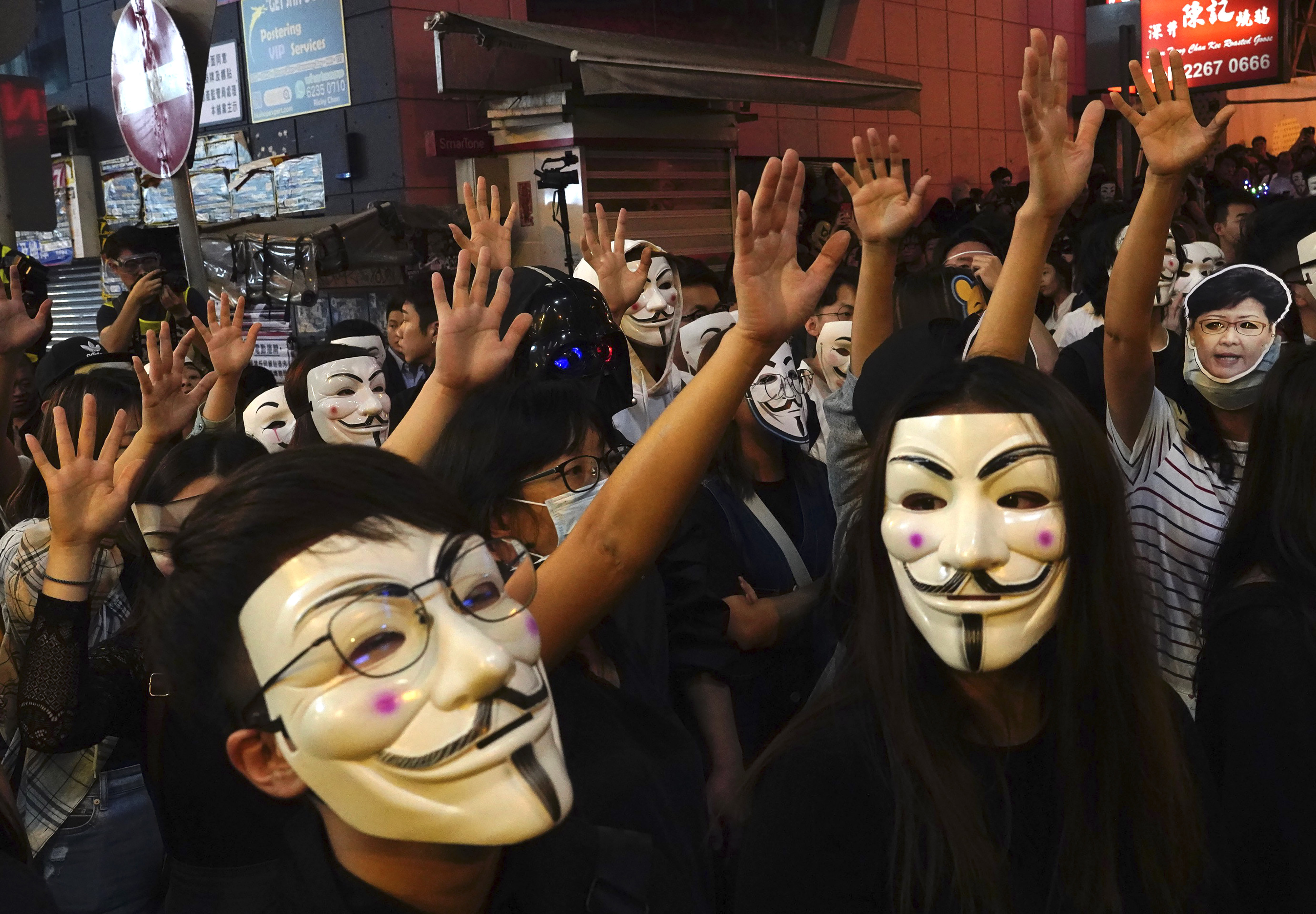 People in Guy Fawkes masks raise their hands as they gather on a street in Hong Kong, Thursday, Oct. 31, 2019. Hong Kong authorities are bracing as pro-democracy protesters urged people on Thursday to celebrate Halloween by wearing masks on a march in defiance of a government ban on face coverings. (AP Photo/Vincent Yu)