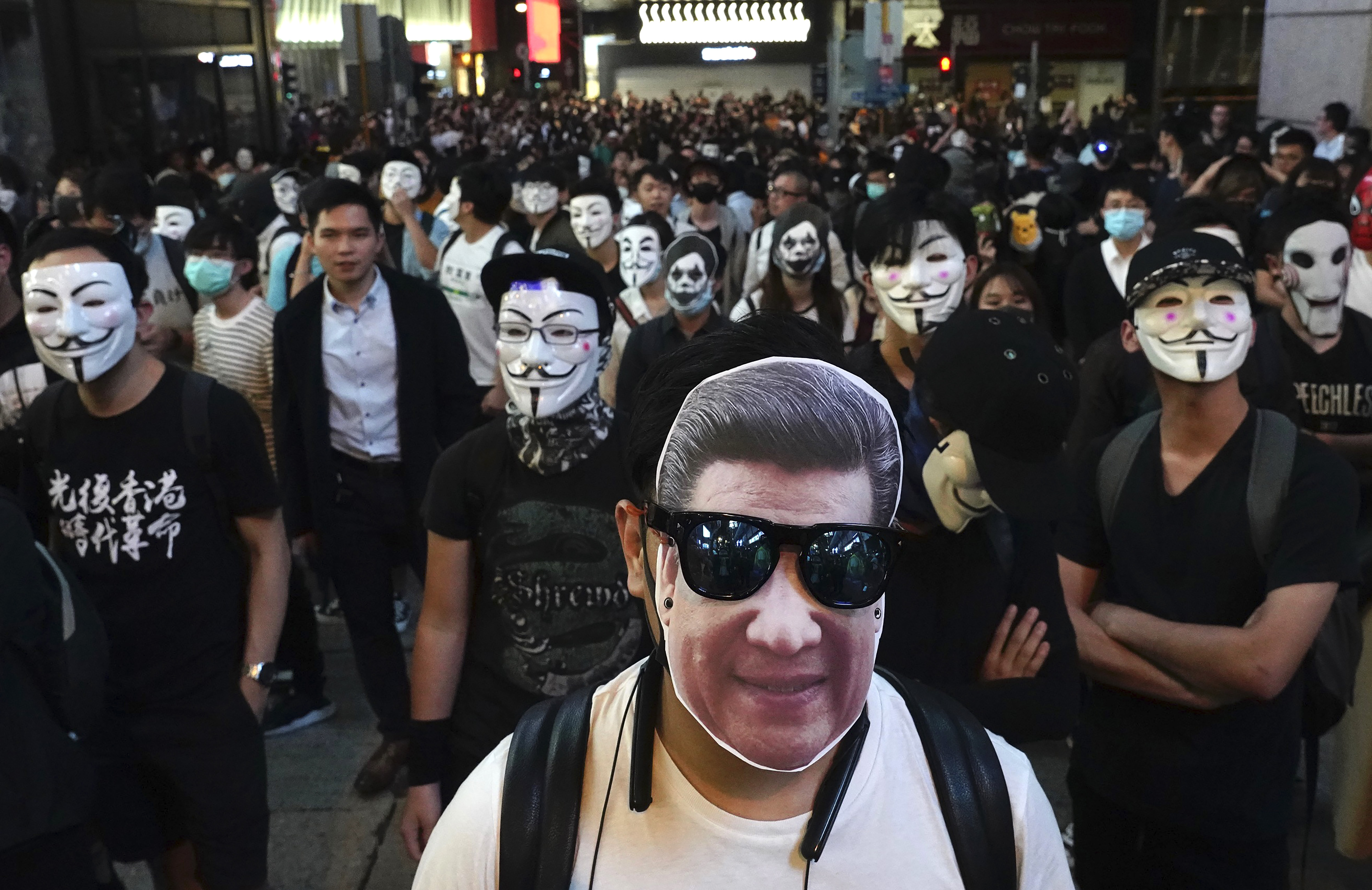 A man wearing a mask of Chinese President Xi Jinping stands with peole wearing Guy Fawkes masks on a street in Hong Kong, Thursday, Oct. 31, 2019. Hong Kong authorities are bracing as pro-democracy protesters urged people on Thursday to celebrate Halloween by wearing masks on a march in defiance of a government ban on face coverings. (AP Photo/Vincent Yu)