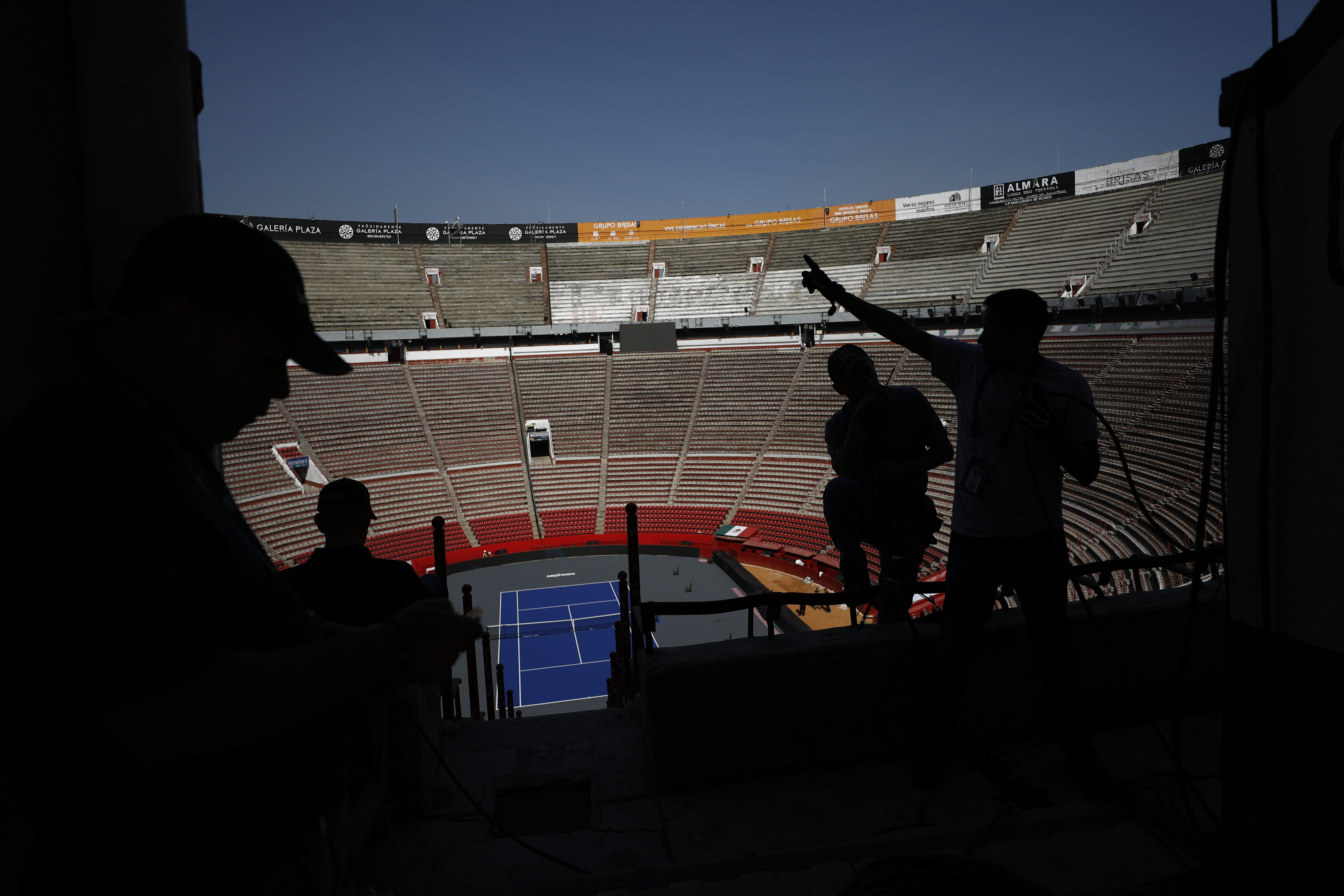 Workers are silhouetted against the Plaza de Toros Mexico bullfighting arena that has been converted to host an exhibition tennis match between Swiss great Roger Federer and German rival Alexander Zverev, in Mexico City, Friday, Nov. 22, 2019. The venue, recognized as the largest bullring in the world, was chosen for the event because it has an estimated 42,000 seating capacity. (AP Photo/Rebecca Blackwell)